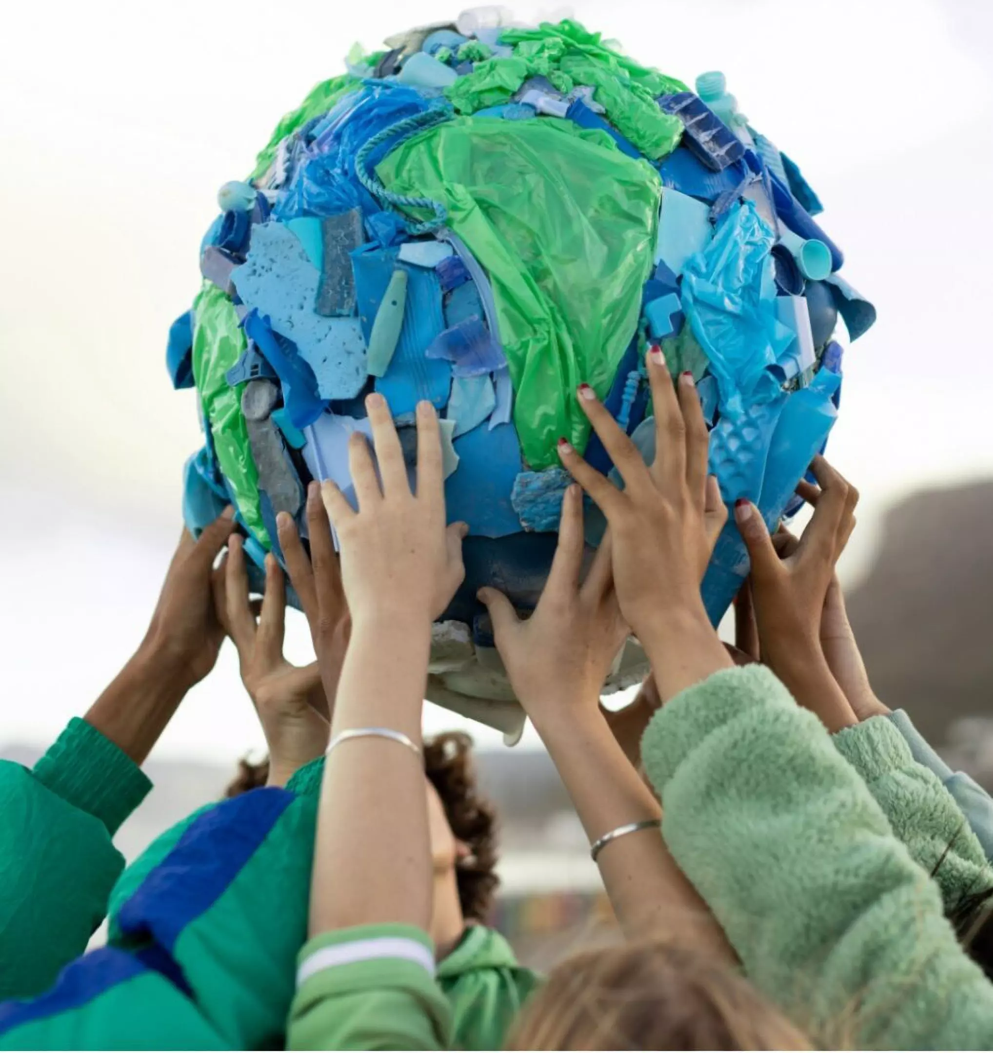 Hands lifting a globe made from recycled plastic in blue and green colors, representing Pepco's environmental initiative.