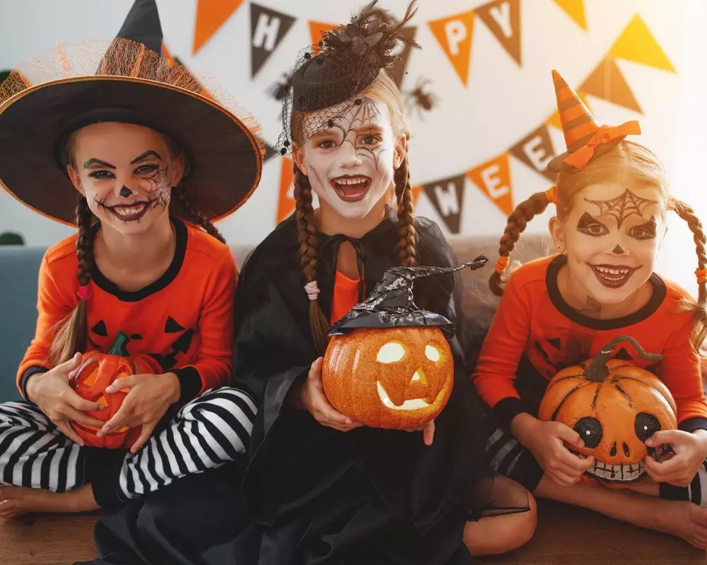 Dzieci w kostiumach Halloween z Pepco, trzymające dynie dekoracyjne, na tle girlandy z flagami HAPPY HALLOWEEN.
