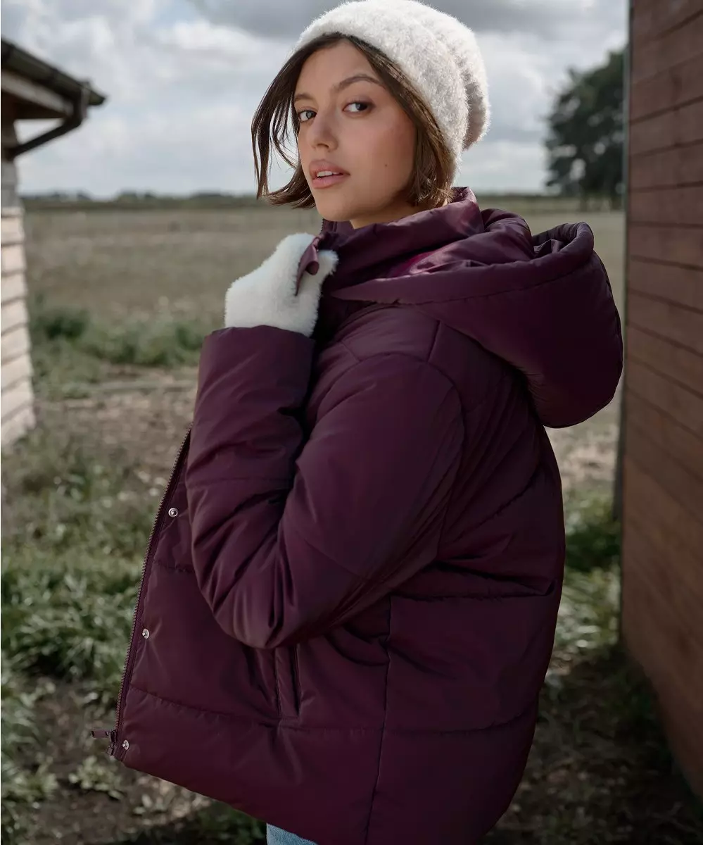 Modelo con abrigo acolchado y gorro blancos de Pepco, posando al aire libre.