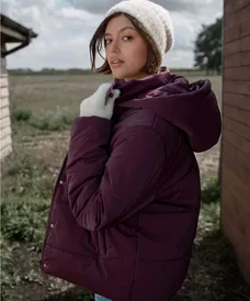 Modelo con abrigo acolchado y gorro blancos de Pepco, posando al aire libre.