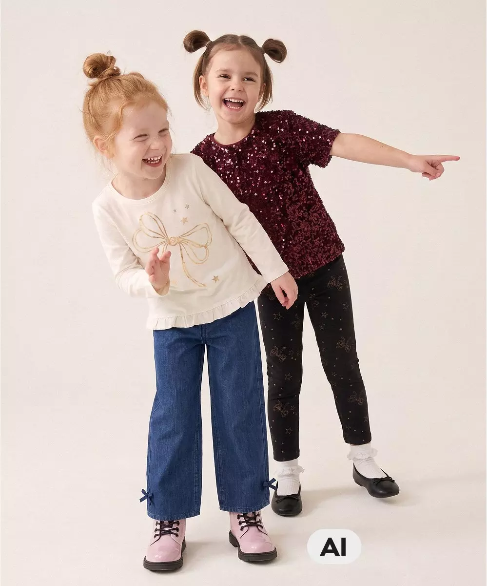 Due bambine sorridenti indossano abbigliamento festivo Pepco con top decorati e pantaloni.