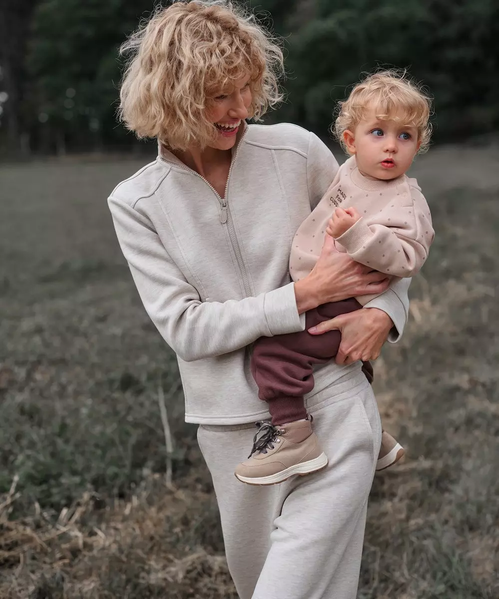 Pepco donna in tuta tiene in braccio un bimbo con felpa e pantaloni.