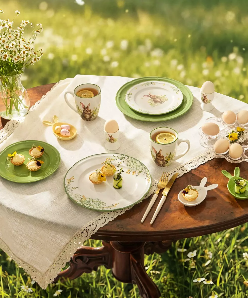 Wielkanocne nakrycie stołu z zastawą ozdobioną motywami króliczków, jajka, herbata z cytryną i drobne przekąski na łące.