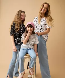 Kobieta i dwie dziewczynki w pasujących bluzach w kropki i dżinsach pozują razem uśmiechnięte.