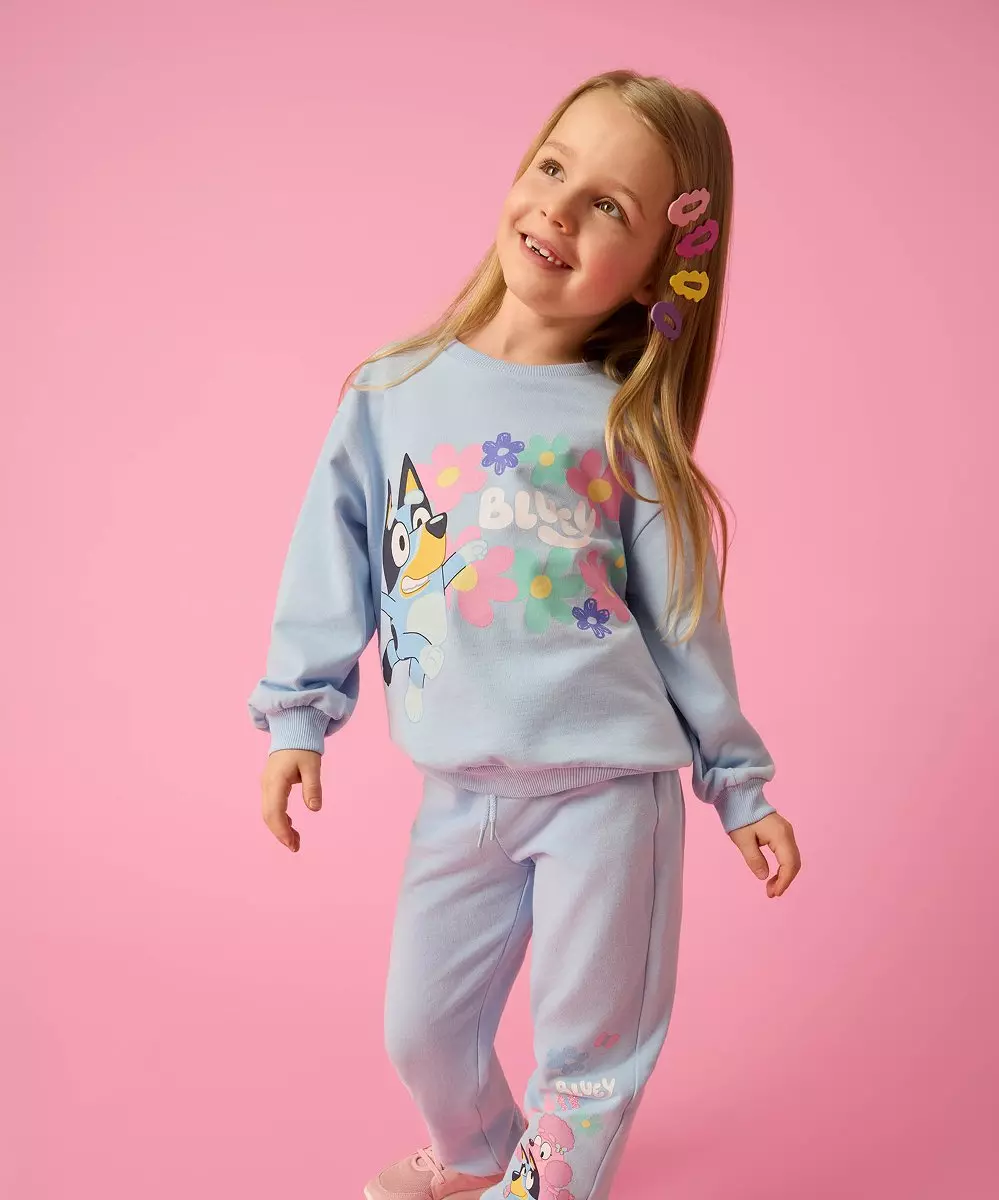 Dziewczynka w niebieskim dresie Bluey z kolorowymi klipsami do włosów, uśmiechająca się.