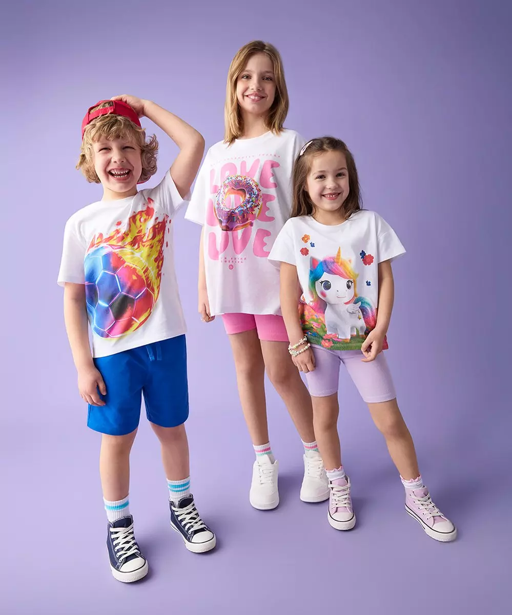 Troje uśmiechniętych dzieci w kolorowych koszulkach z grafiką i szortach, pozujących razem.