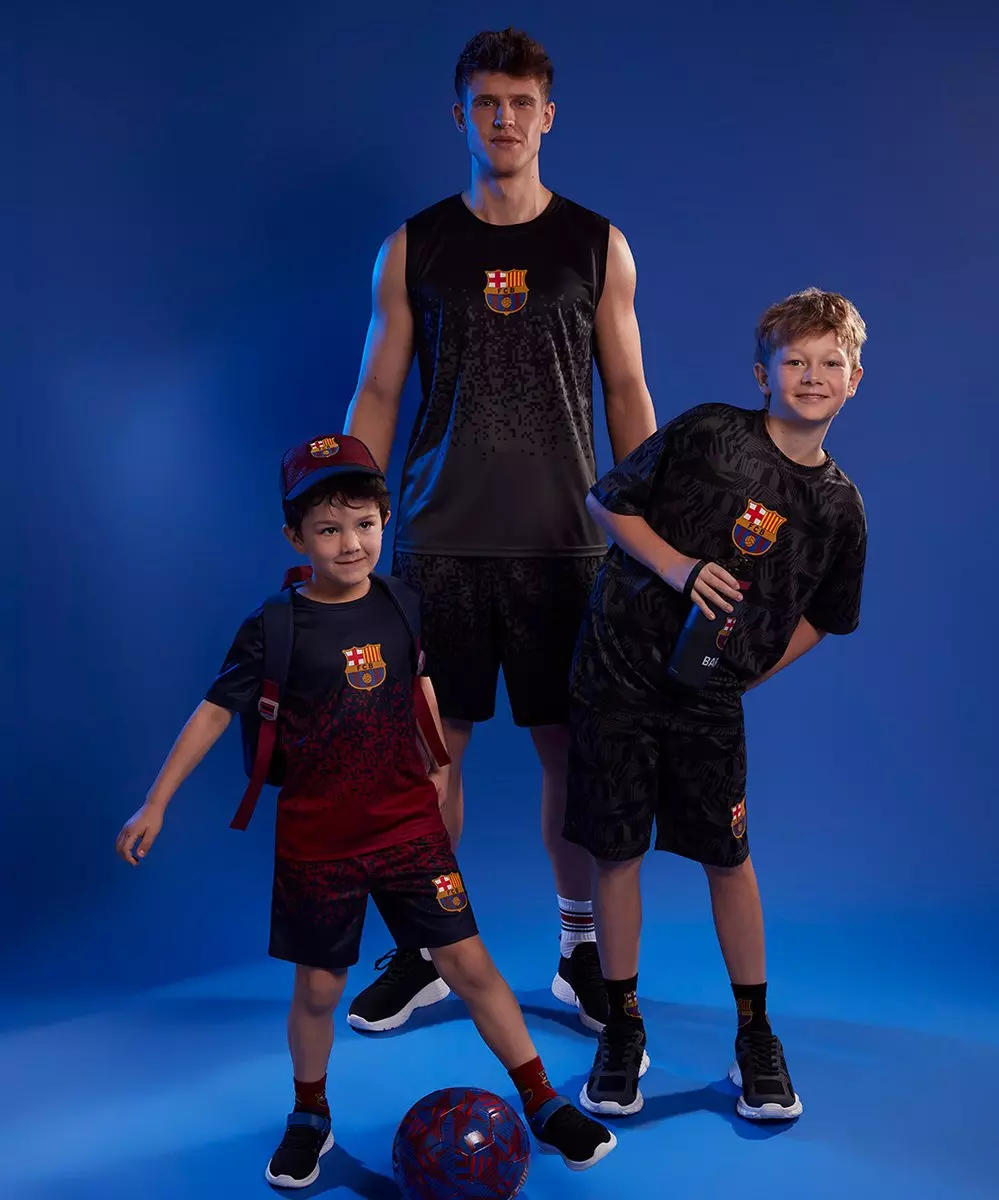 Muž a dva chlapci v sportovním oblečení FC Barcelona s fotbalovým míčem.