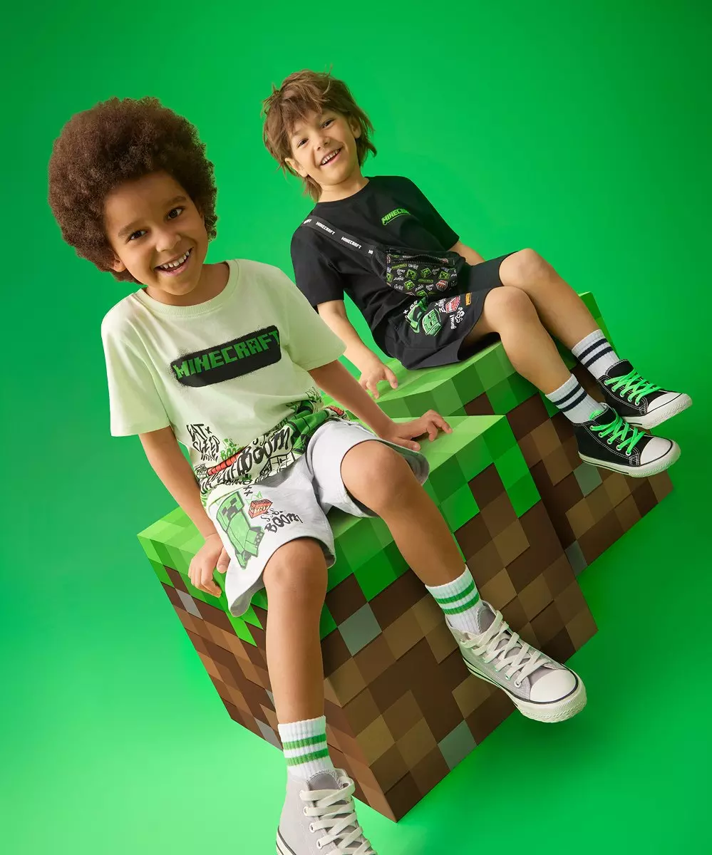 Dos niños sonrientes sentados en bloques pixelados, vistiendo ropa y zapatillas de Minecraft.