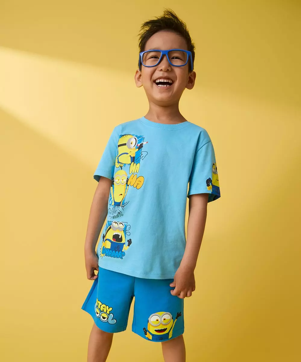 Pepco boy wearing blue glasses, smiling in a light blue Minions t-shirt and matching blue Minions shorts.
