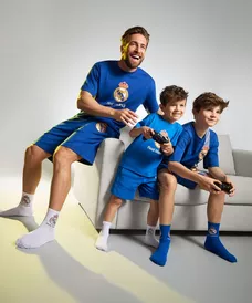 Padre e hijos vistiendo pijamas azules del Real Madrid de Pepco mientras juegan videojuegos en el sofá.