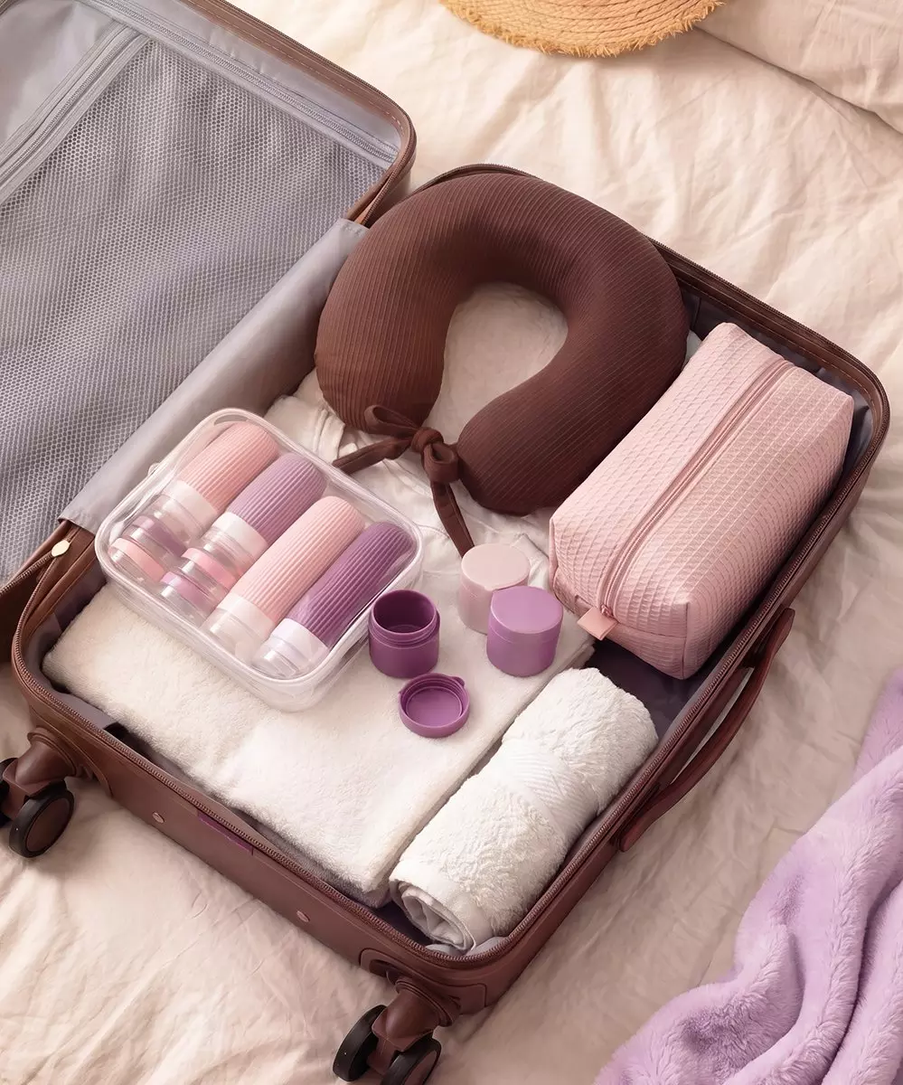 Maleta Pepco organizada con almohada de viaje, neceser rosa, botellas de viaje y toallas para vacaciones.