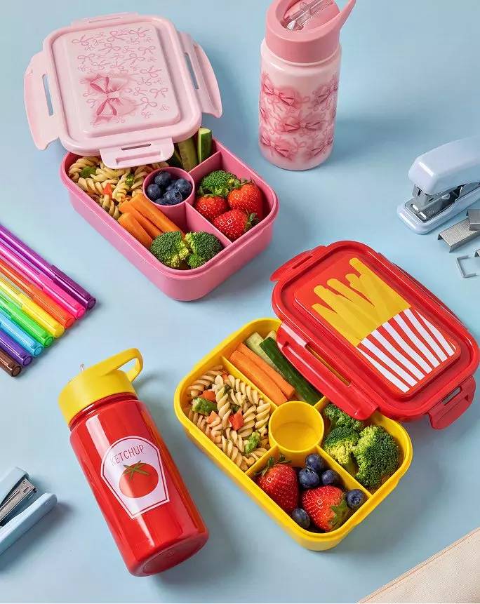Cutii de prânz Pepco roz și galbene cu fructe, legume și paste, alături de sticle colorate și rechizite.