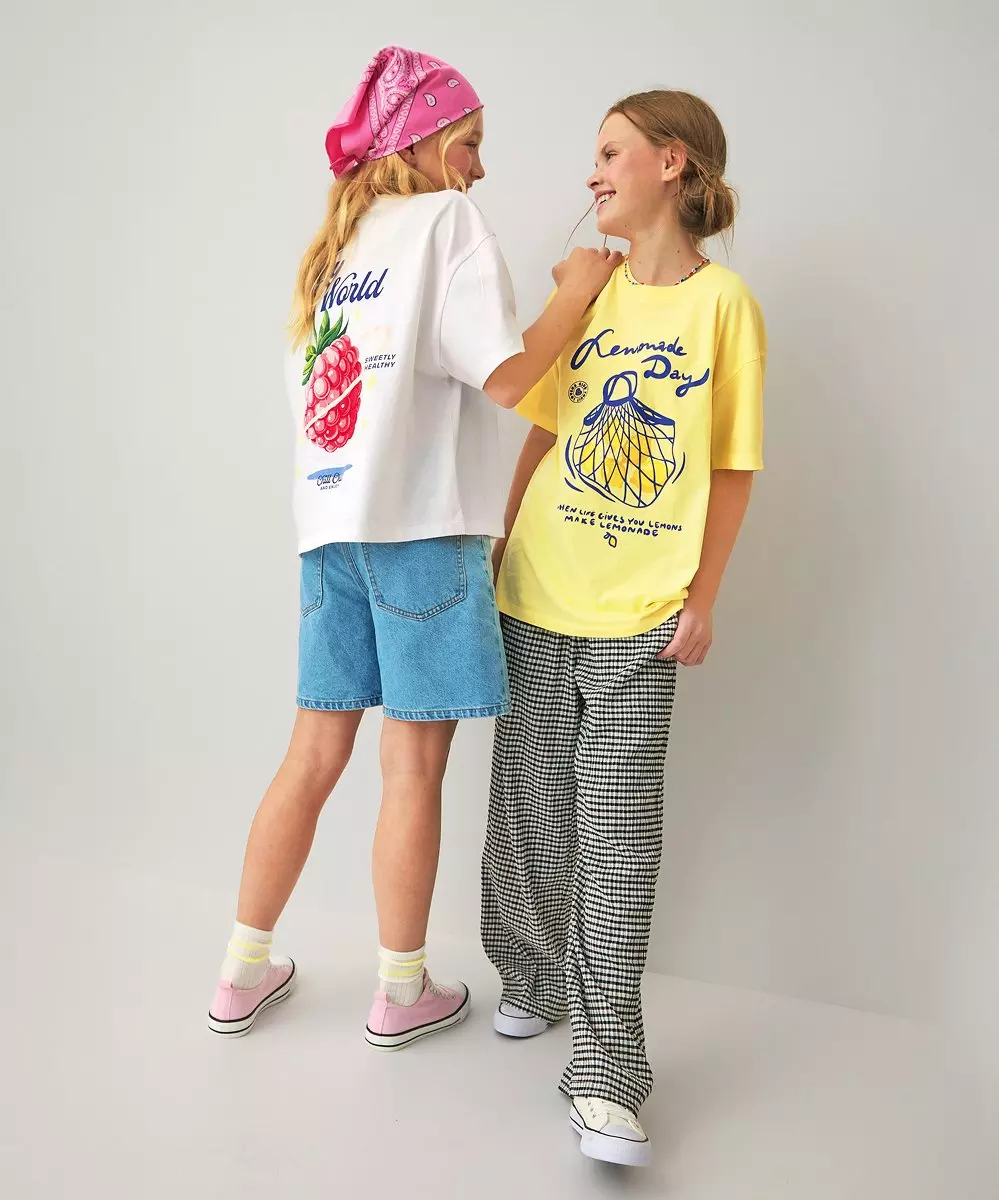 Dwie dziewczyny rozmawiają, ubrane w kolorowe t-shirty z nadrukami owoców i tekstem.