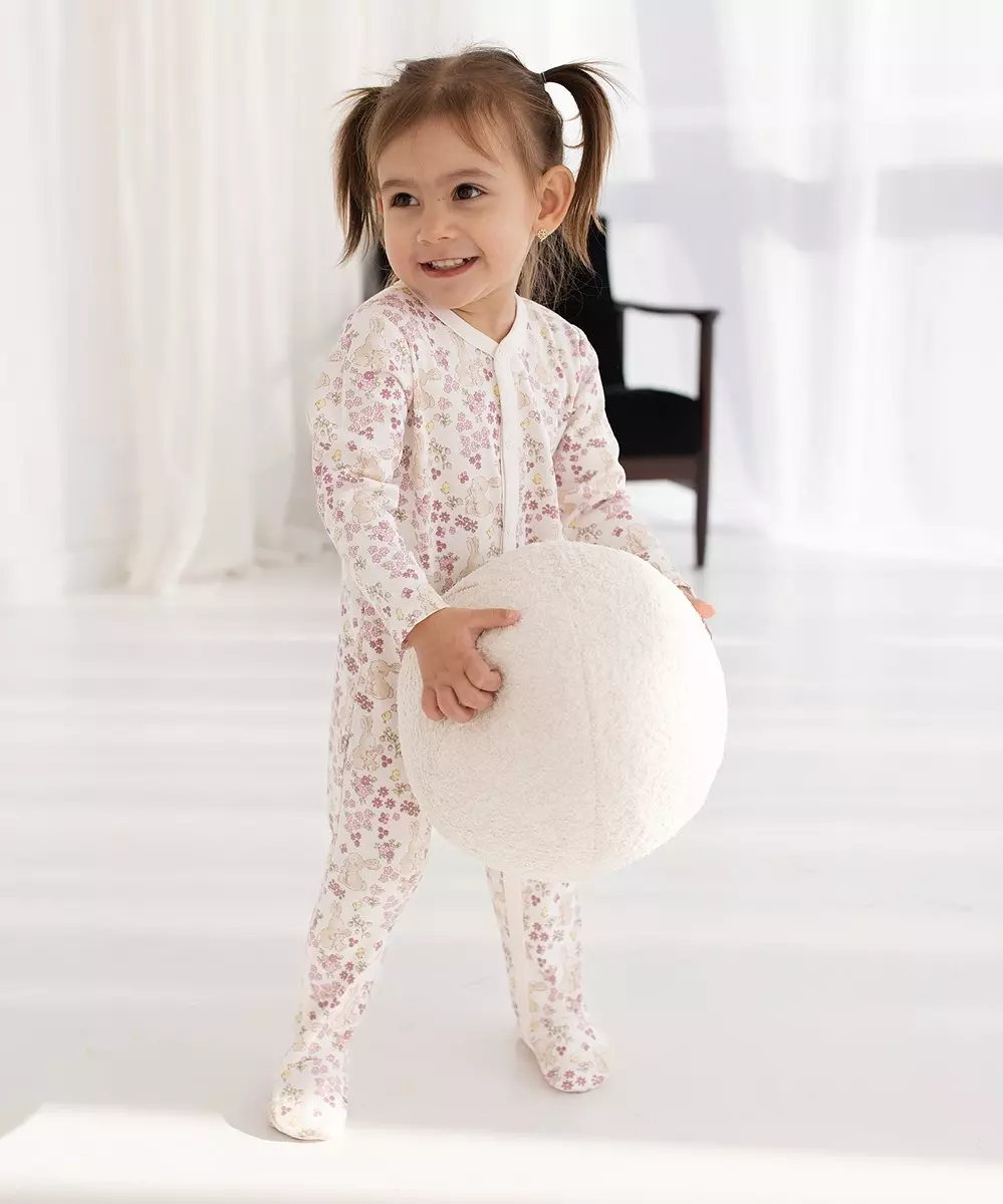 Uśmiechnięta dziewczynka w piżamie w kwiatowy wzór trzymająca białą poduszkę.