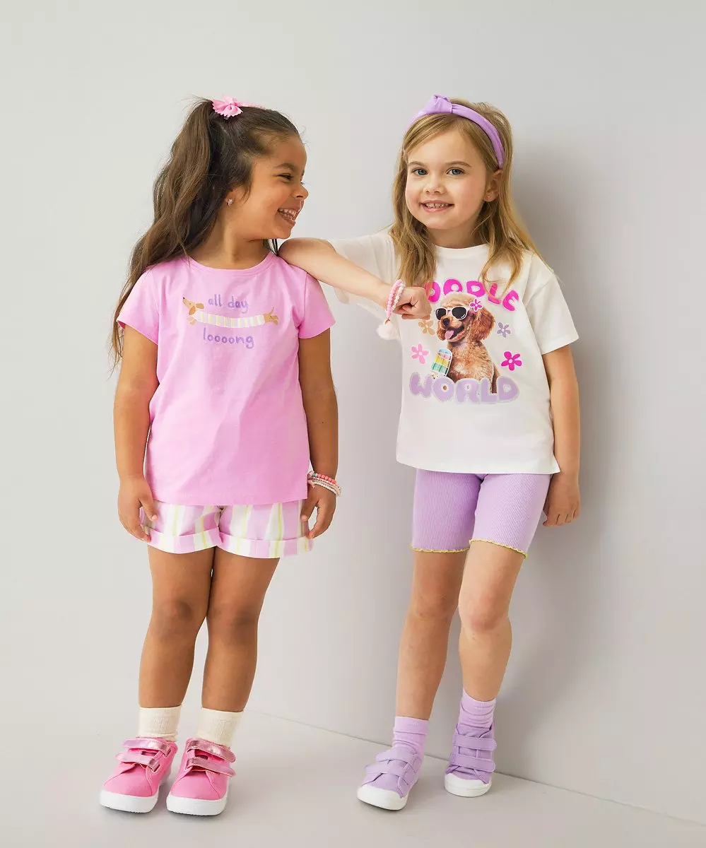 Dwie dziewczynki w kolorowych strojach z nadrukami stojące razem i uśmiechające się.