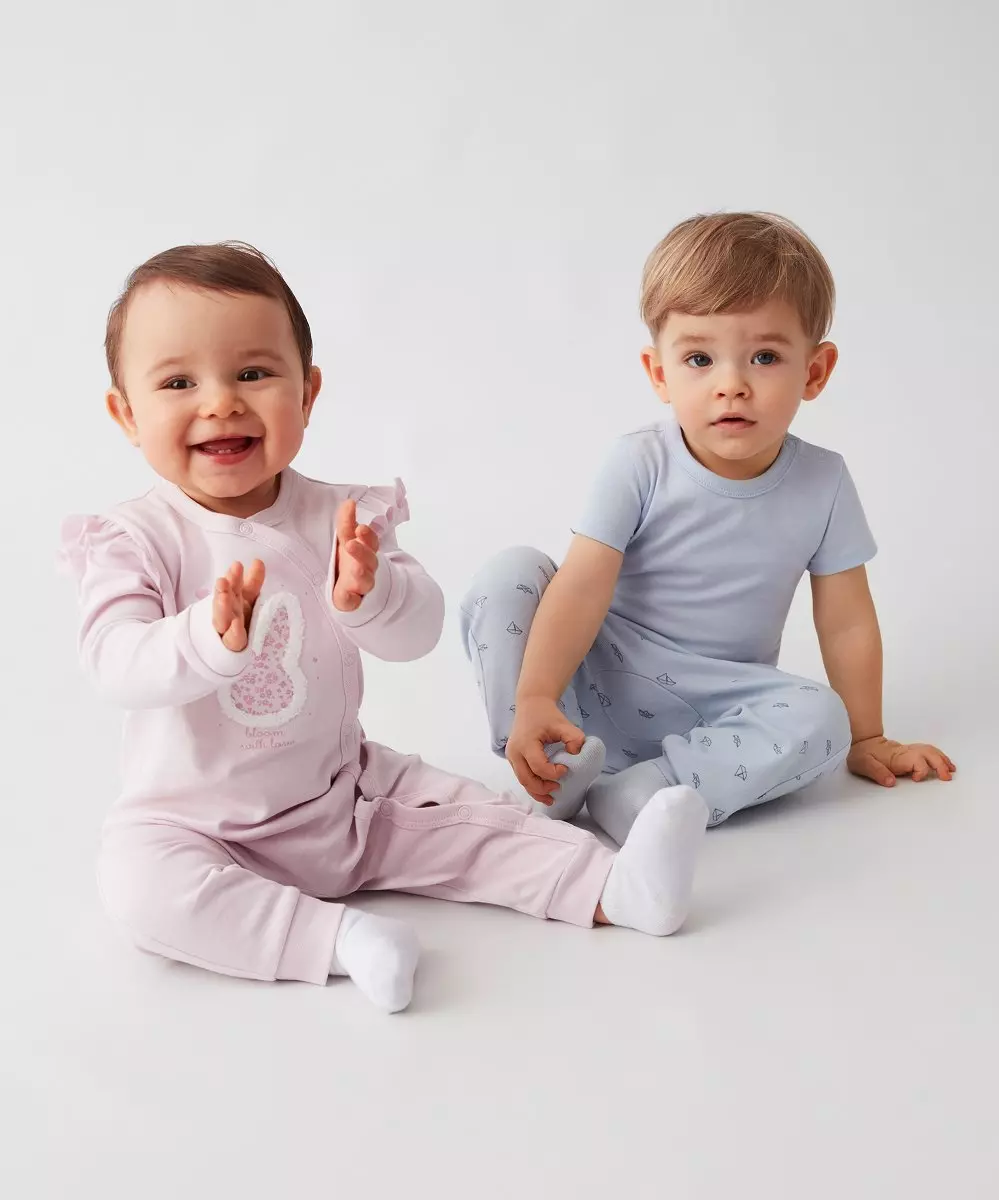 Two toddlers wearing sleepwear, one in pink with bunny design and one in light blue with small patterns.