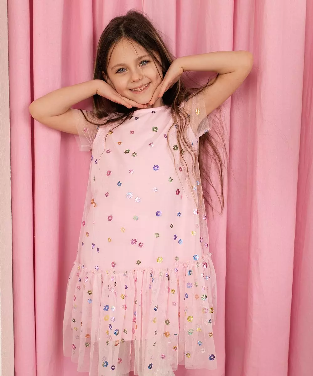 Dziewczyna w różowej sukience z tiulowymi rękawami i kolorowymi kwiatowymi aplikacjami.