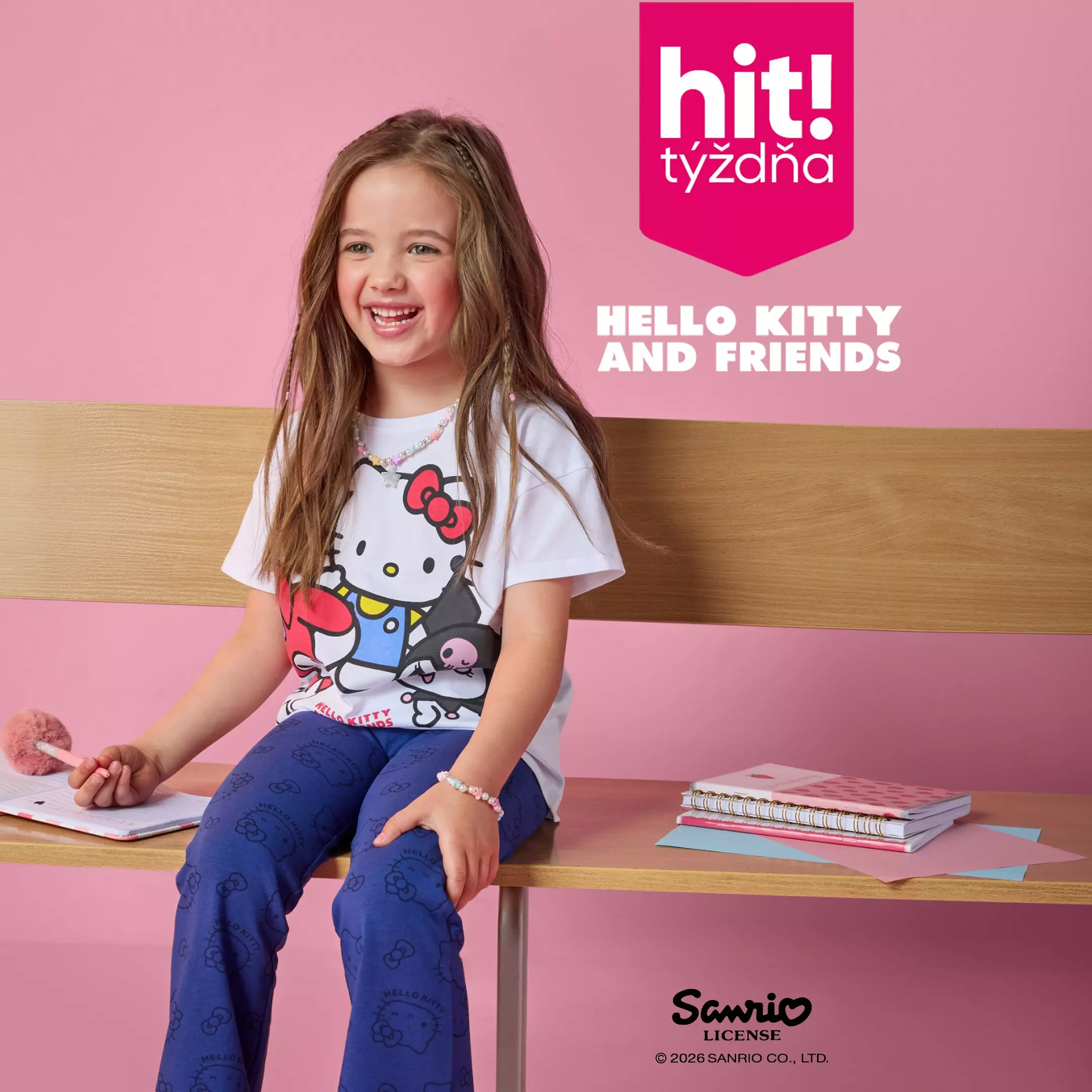 Dievča sedí na stole v Pepco oblečení s motívom Hello Kitty, vrátane bieleho trička a modrých nohavíc.