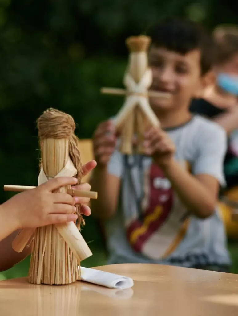 Copii creând păpuși din paie și lemn într-un atelier de lucru manual.