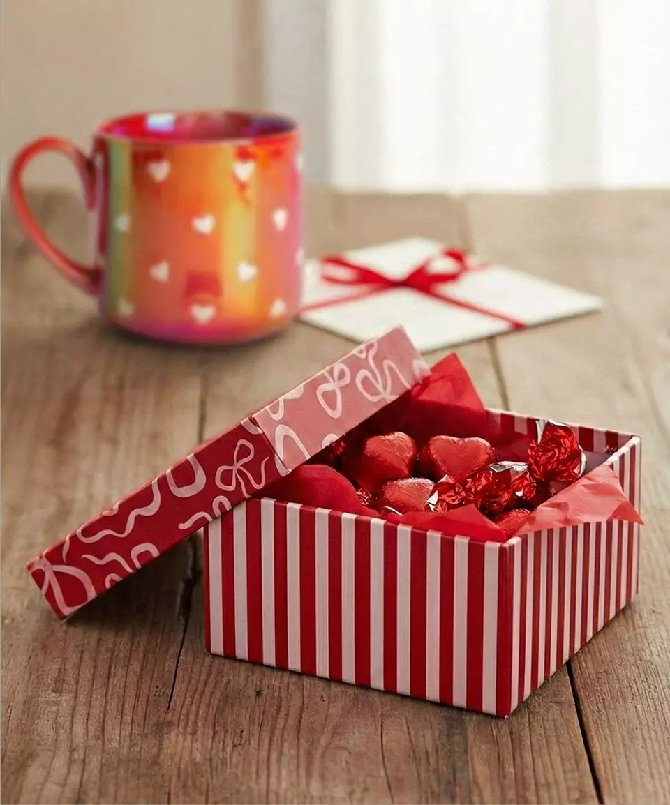 Pepco Valentine's gift box with heart-shaped chocolates next to a colorful heart-patterned mug and envelope on wooden table.