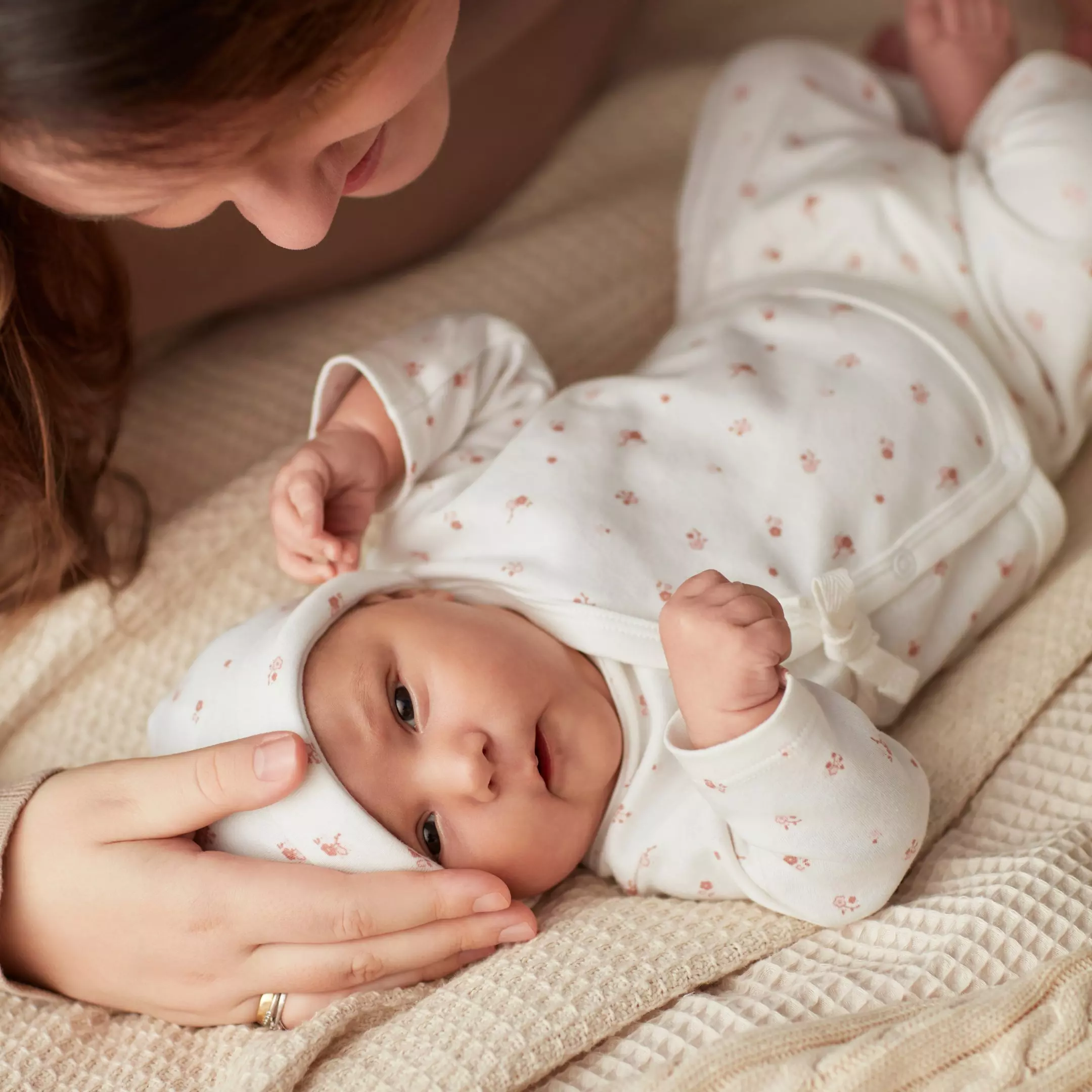 Kobieta opiekuje się niemowlęciem ubranym w biały komplet z drobnym wzorem w kwiatki.