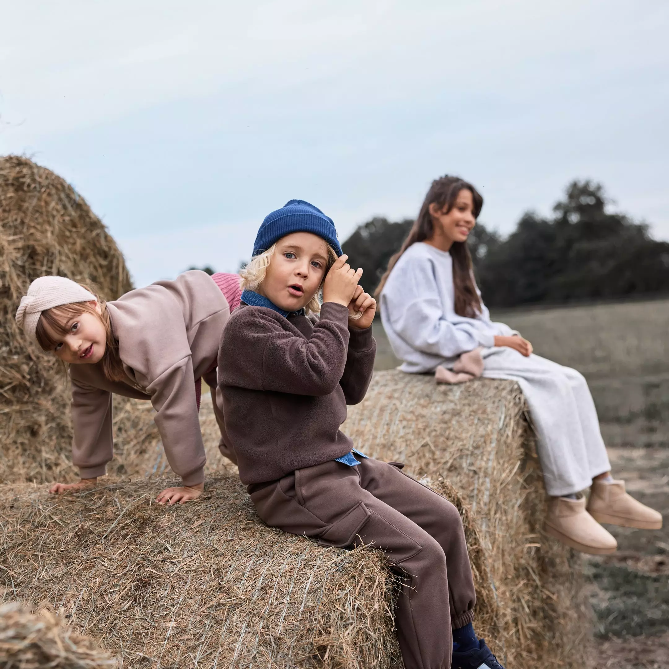 Niños con ropa deportiva Pepco jugando sobre fardos de heno en el campo con una mujer al fondo.