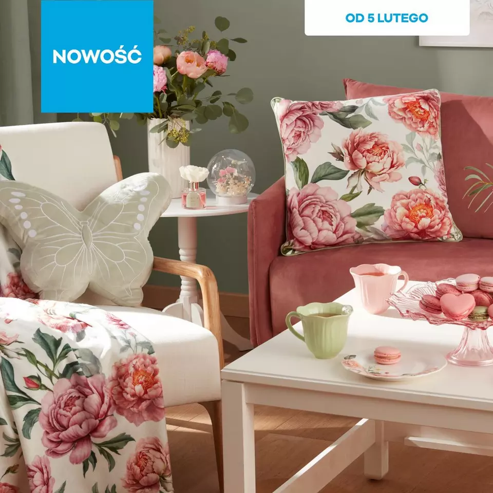 Przytulny salon z różową kanapą, poduszką w kwiaty, fotelem z motylem i stolikiem z makaronikami. Napis "NOWOŚĆ" i "OD 5 LUTEGO".