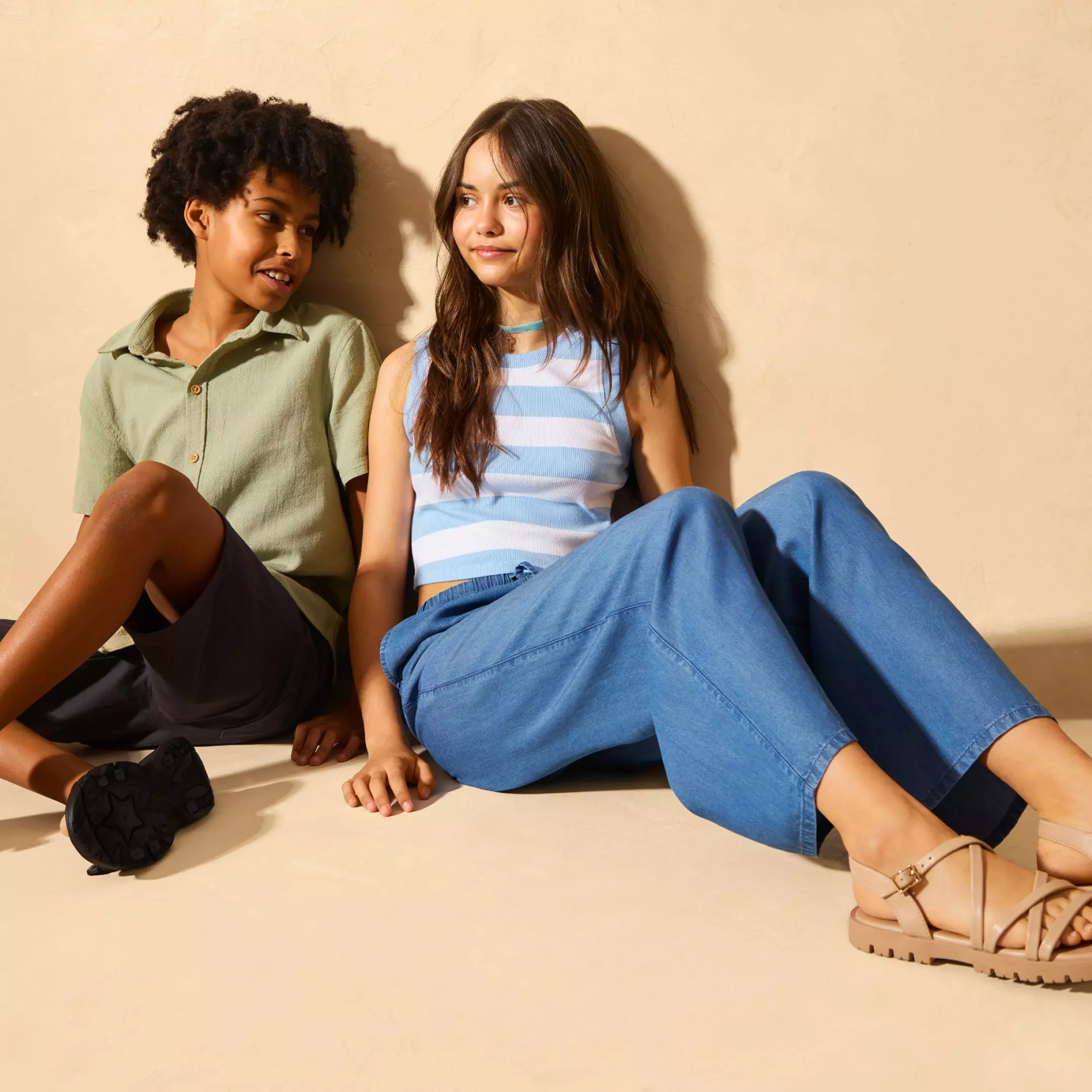 Două femei stau relaxate pe podea, purtând îmbrăcăminte casual de primăvară-vară.