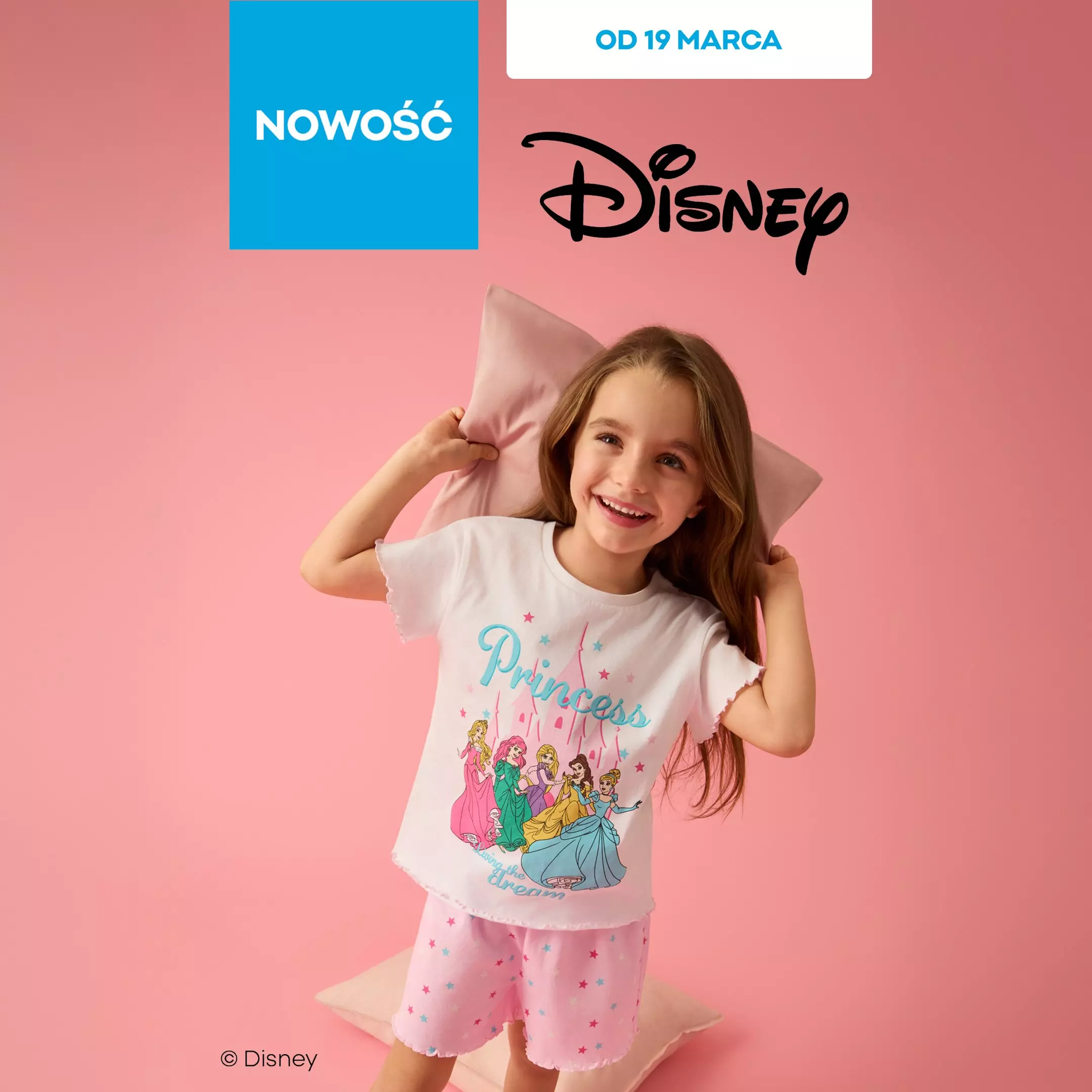 Dziewczynka w piżamie Disney z księżniczkami, trzymająca różową poduszkę i uśmiechająca się.