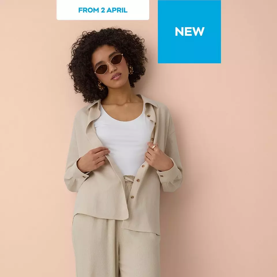 Woman wearing beige linen suit with white top and sunglasses, styled with gold earrings.