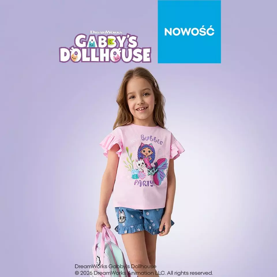 Dziewczynka w różowej koszulce Gabby's Dollhouse z nadrukiem postaci i niebieskich szortach.