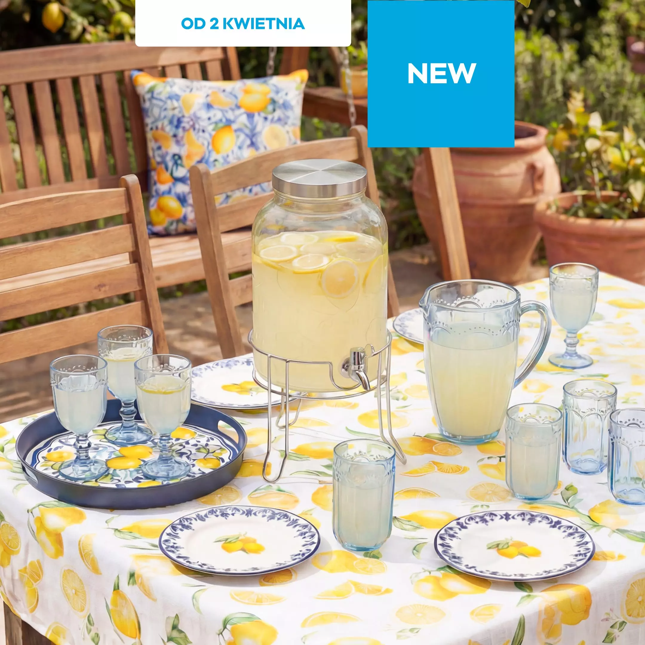 Outdoor table set with lemon-themed tableware, glass beverage dispenser filled with lemonade, and glasses.