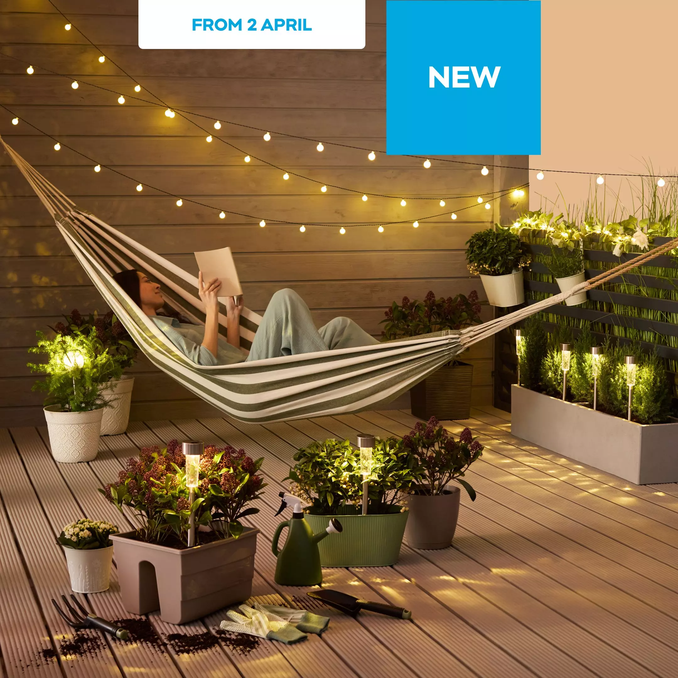 Person relaxing in striped hammock reading a book on wooden deck with string lights and potted plants.
