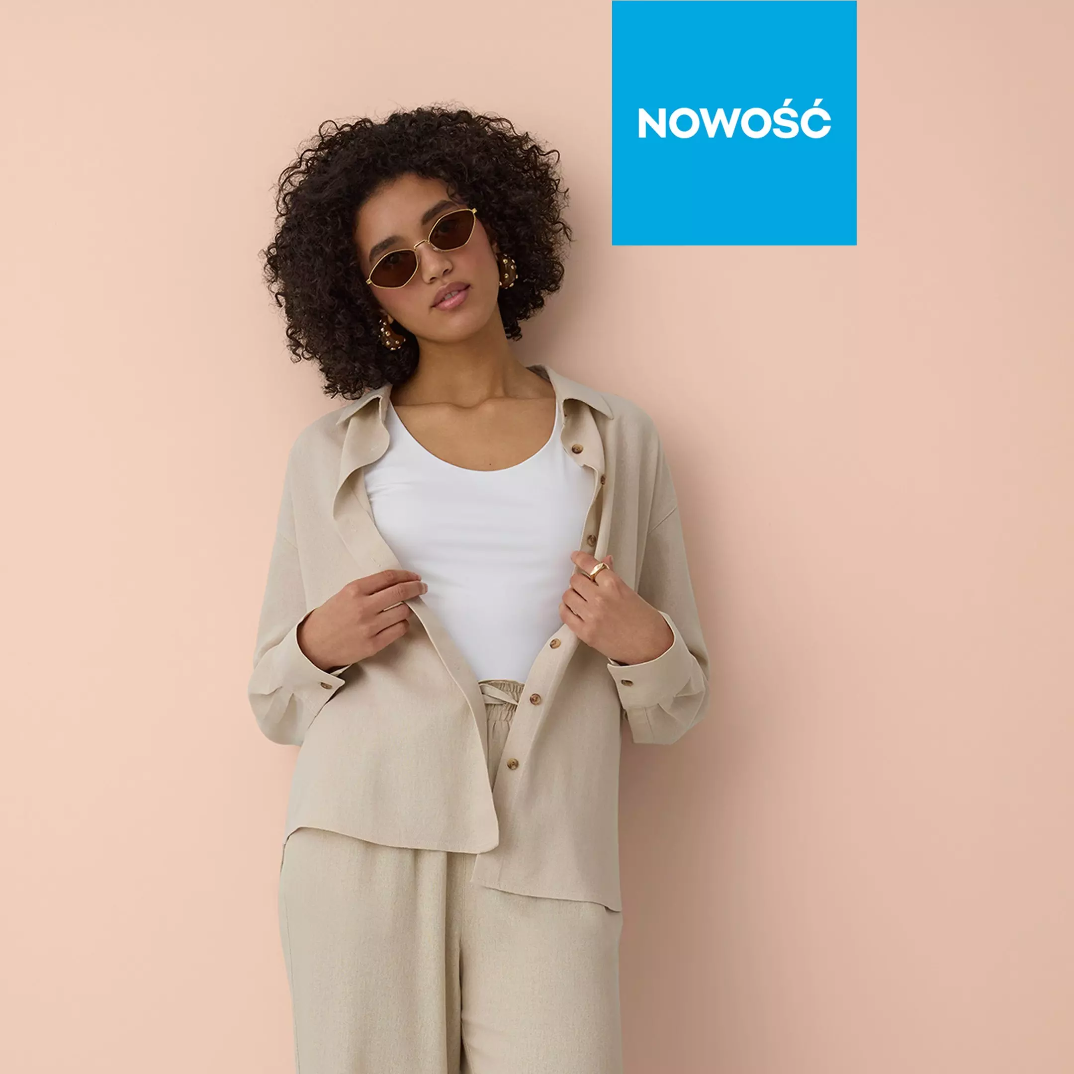 Kobieta w beżowym lnianym garniturze i okularach przeciwsłonecznych z napisem NOWOŚĆ.