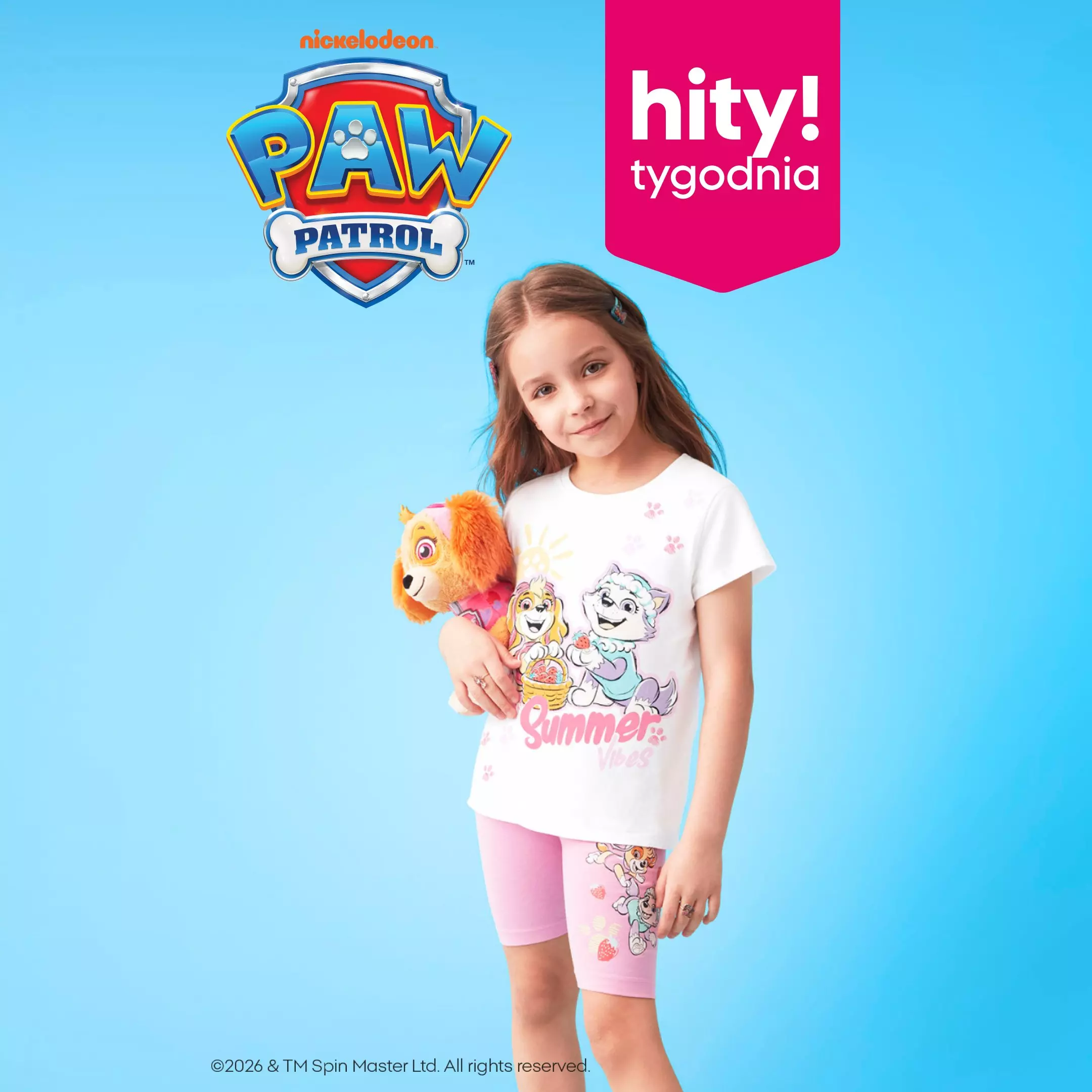 Dziewczynka w białej koszulce i różowych szortach z motywem Psi Patrol, trzymająca pluszową zabawkę.