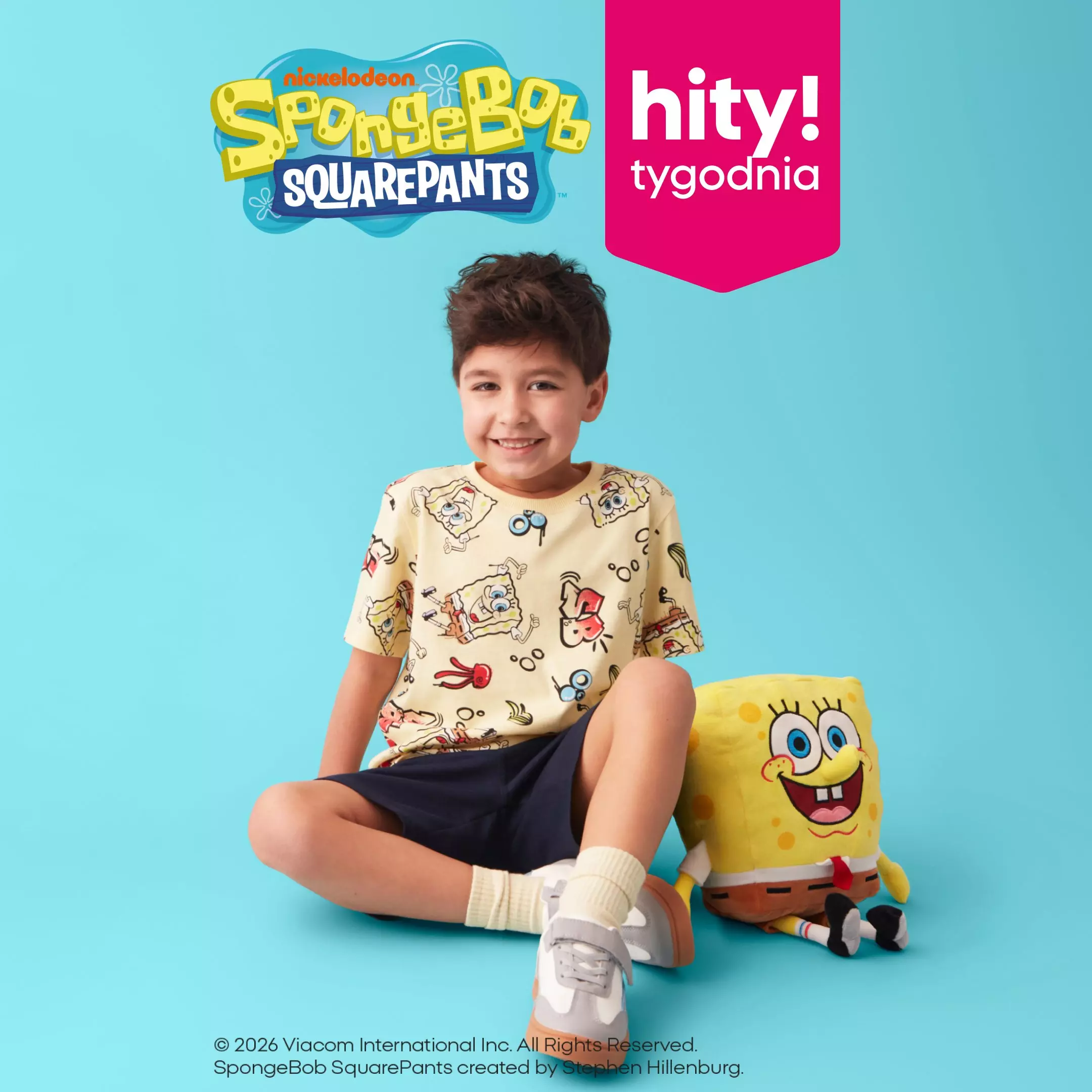 Chłopiec w żółtej koszulce z nadrukiem SpongeBob SquarePants siedzi obok pluszaka SpongeBoba.