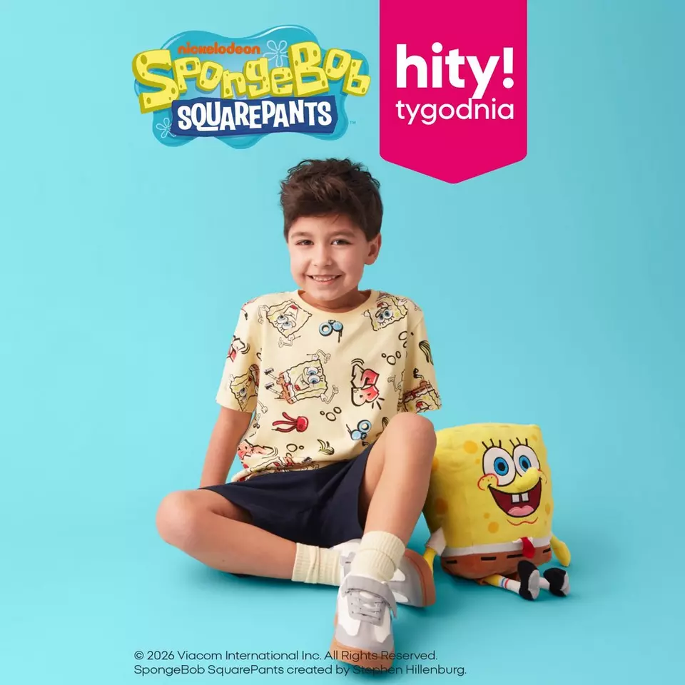 Chłopiec w żółtej koszulce z nadrukiem SpongeBob SquarePants siedzi obok pluszaka SpongeBoba.