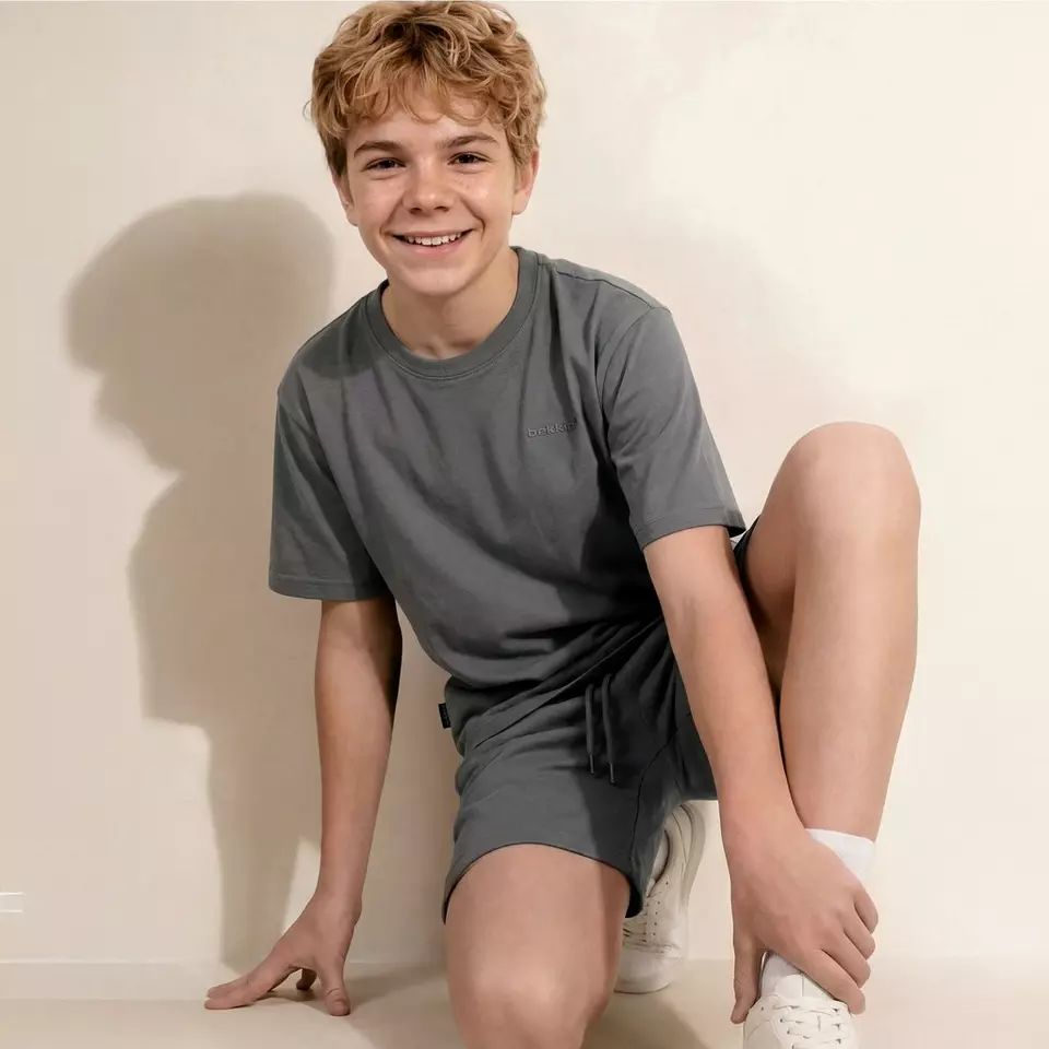 Chlapec v šedém tričku a kraťasech sedí a usmívá se do kamery.