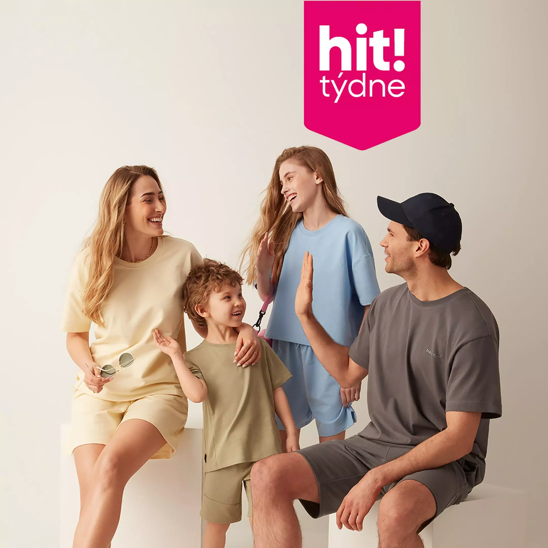 Rodina ve sladěných pastelových tričkách a šortkách značky hit! týdne, usmívající se navzájem.