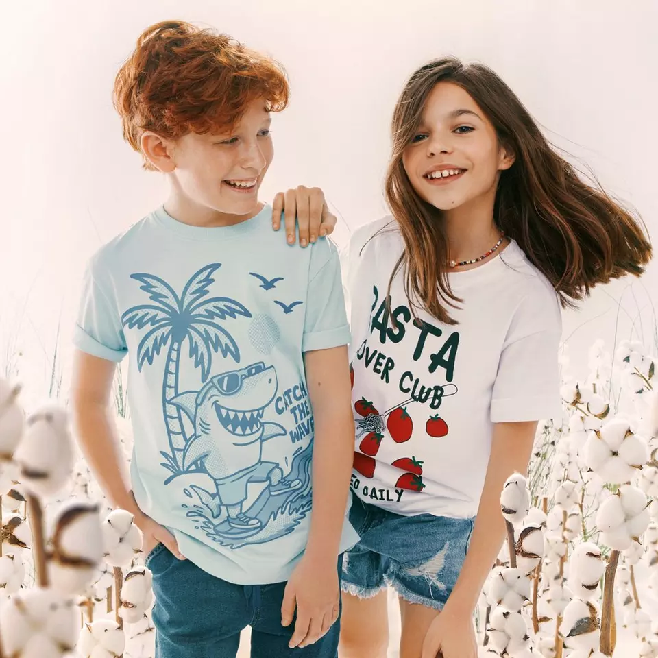 Dos niños sonrientes posando juntos, llevando camisetas estampadas con pantalones vaqueros.