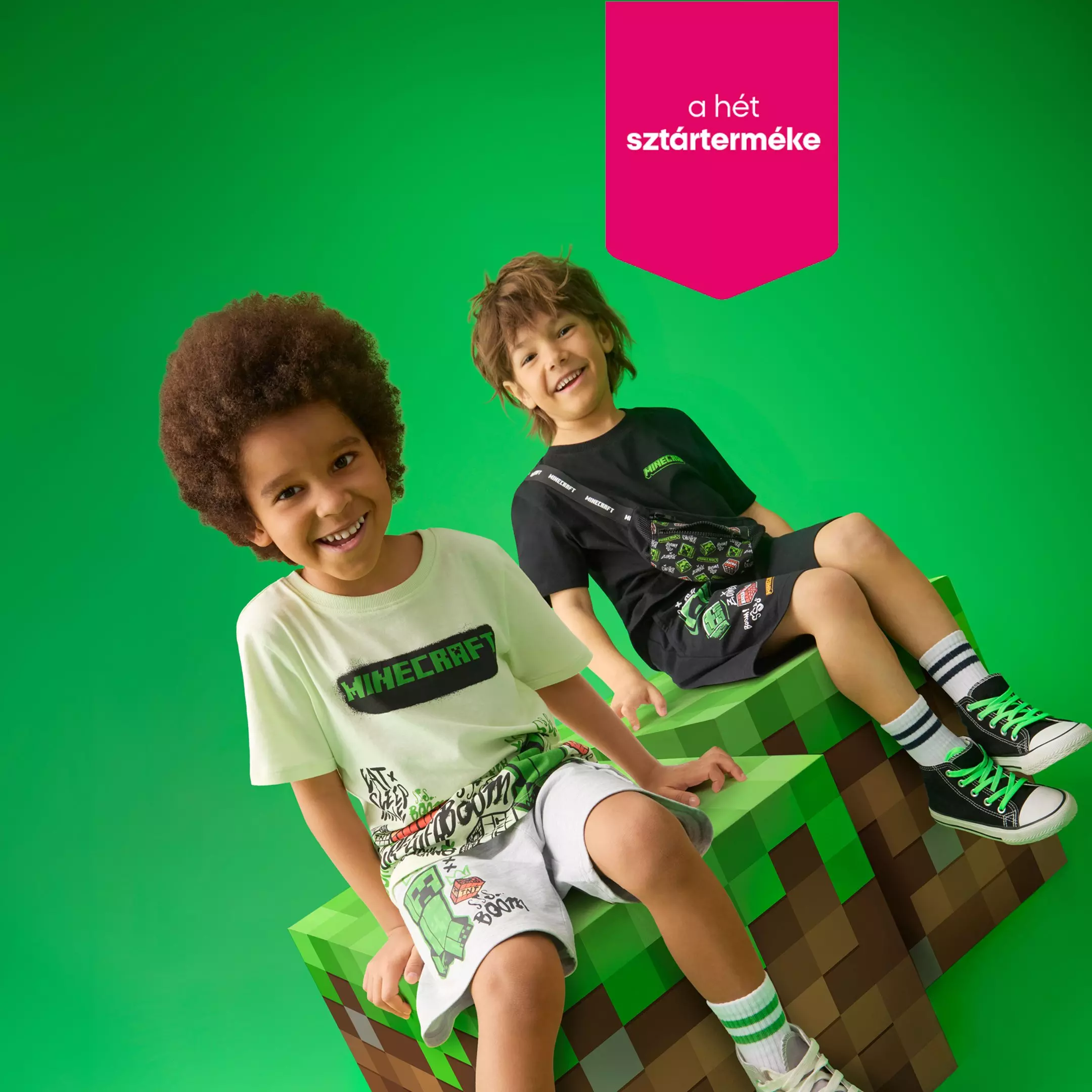 Két mosolygó fiú Minecraft pólóban és cipőben ül egy nagy Minecraft blokkon.