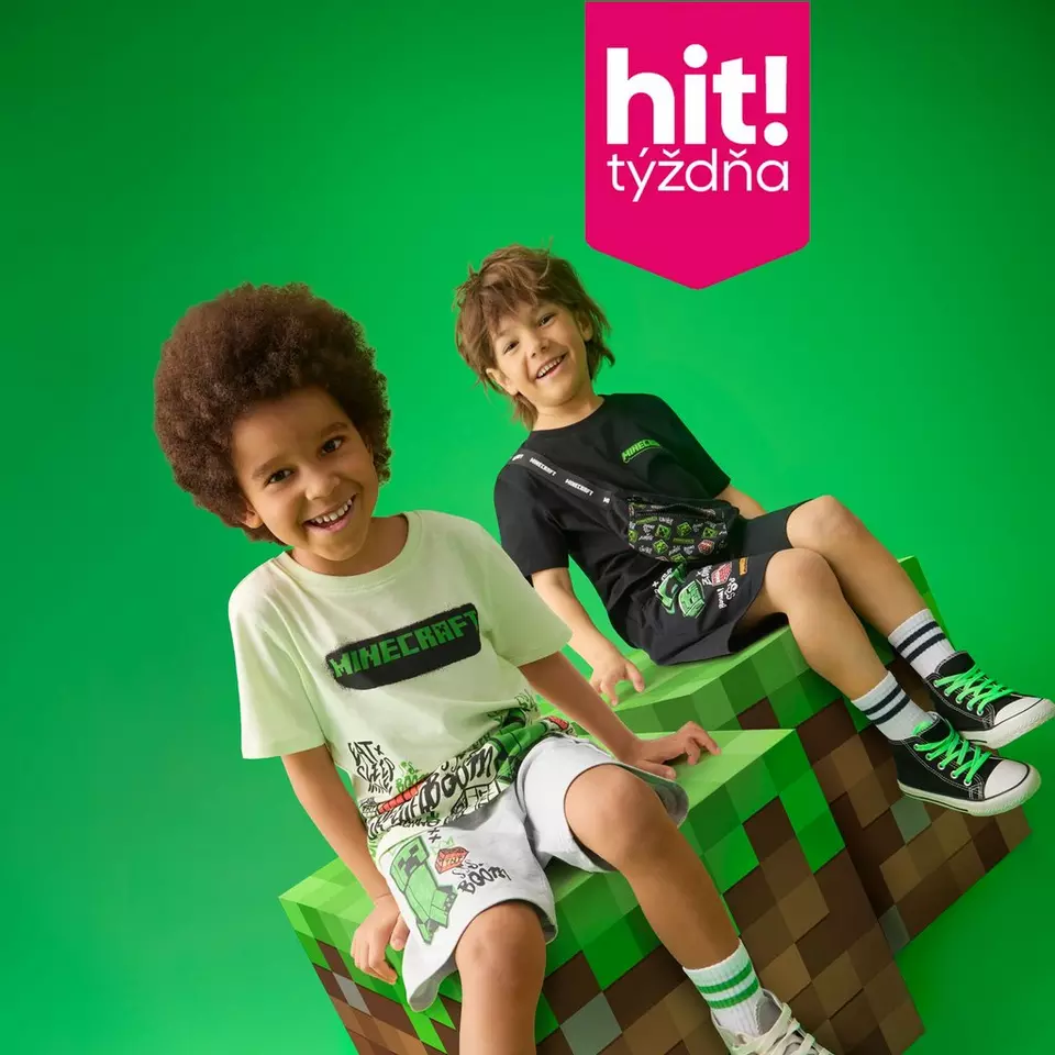 Dvaja chlapci v oblečení s motívom Minecraft sedia na veľkej kocke inšpirovanej hrou a usmievajú sa.