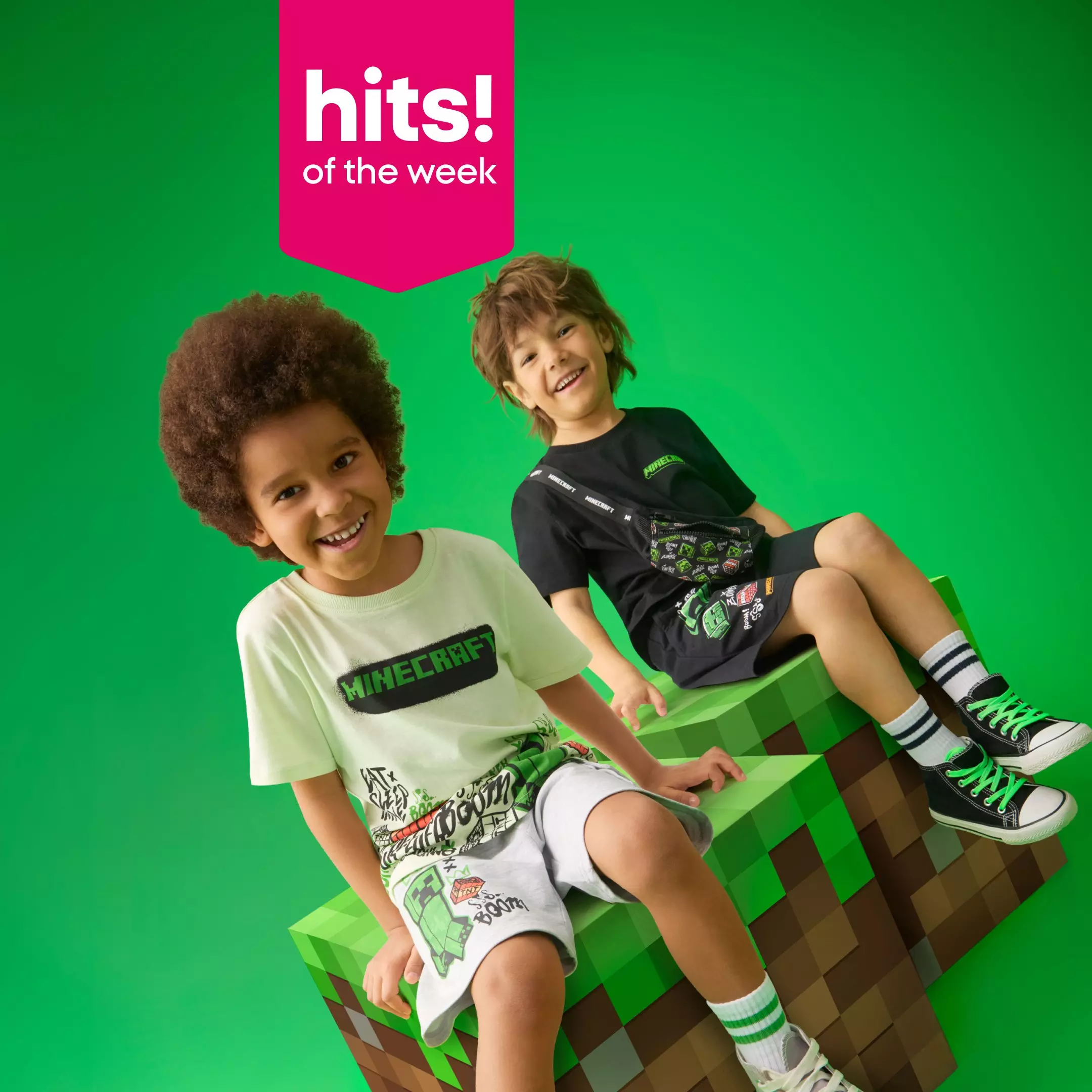 Two smiling boys wearing Minecraft branded clothing and accessories sitting on pixelated blocks.