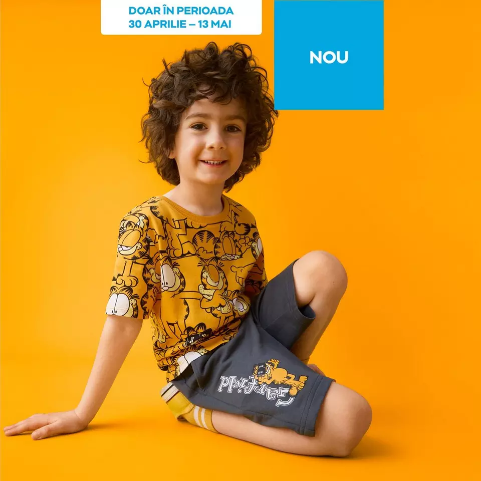 Copil zâmbitor purtând tricou galben cu imprimeu Garfield și pantaloni scurți gri.