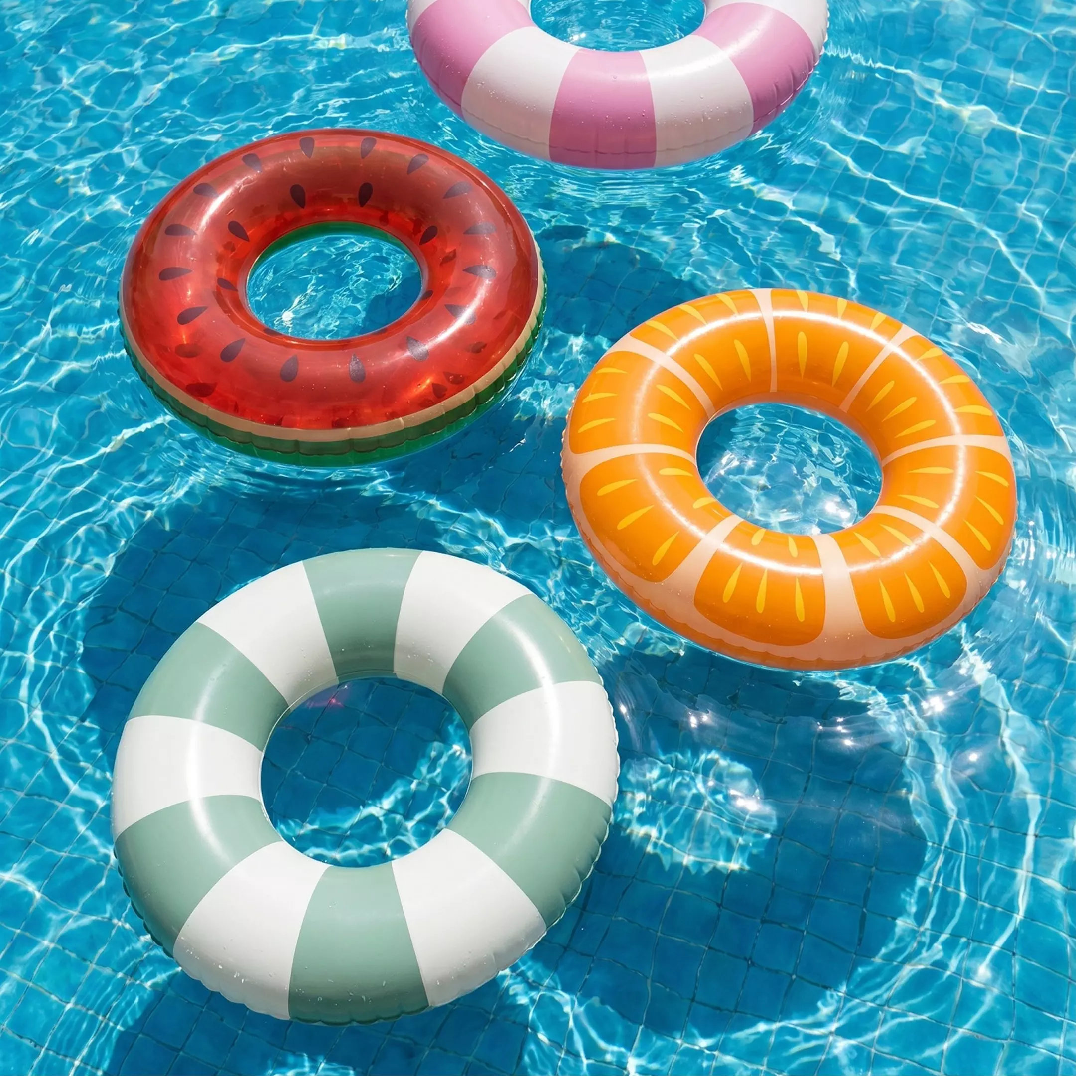Colace gonflabile colorate plutind într-o piscină cu apă albastră, incluzând design pepene verde și portocală.