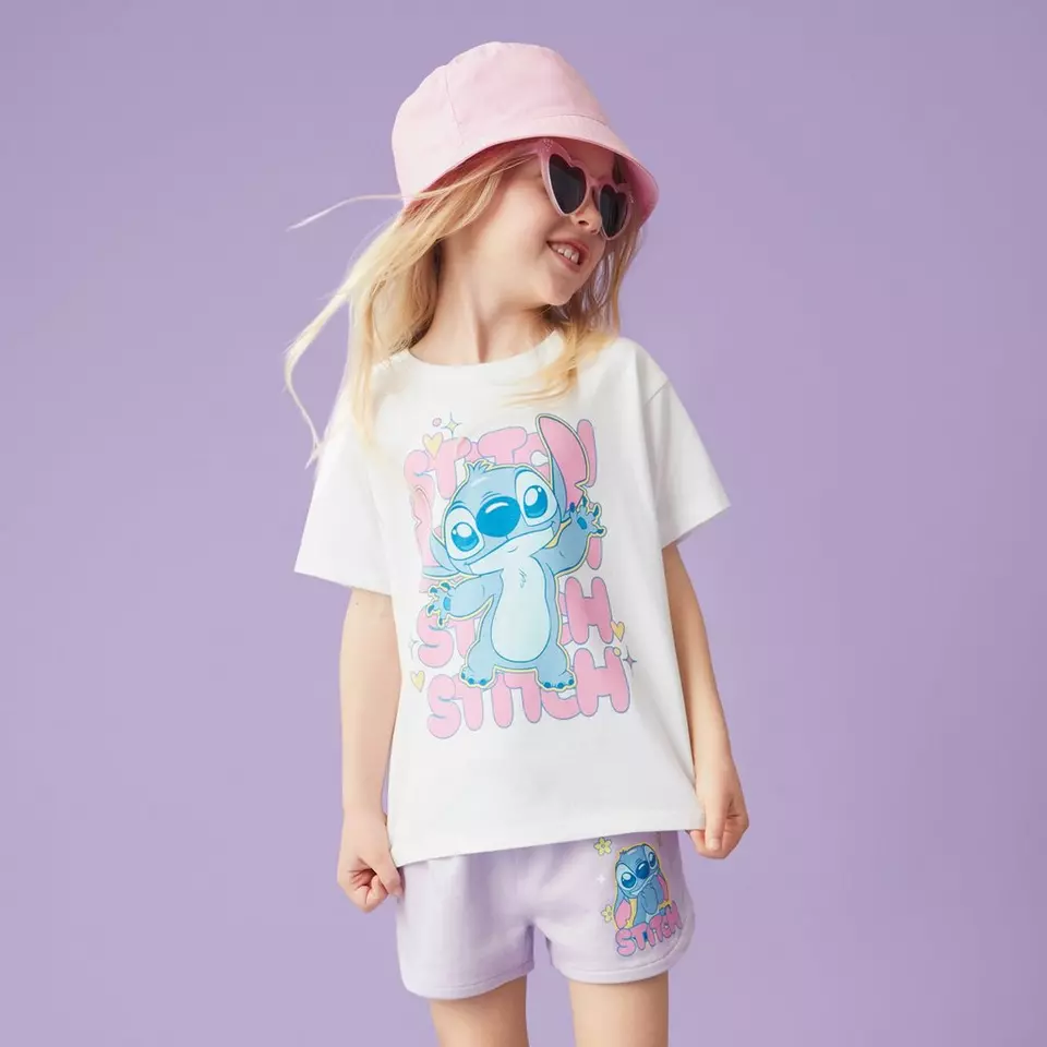 Fetiță purtând tricou alb cu Stitch, pălărie roz și ochelari de soare în formă de inimă.