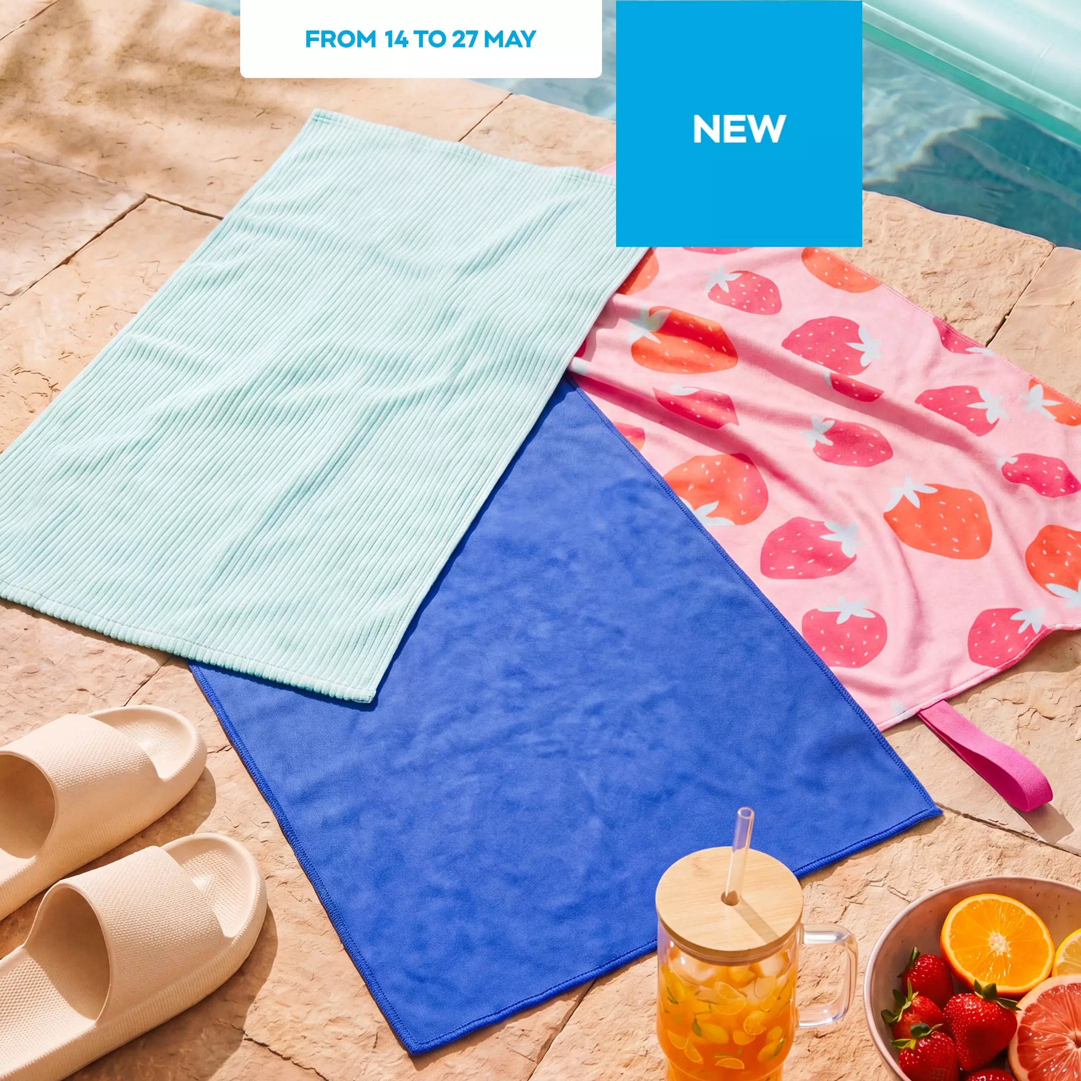 Three colourful beach towels displayed poolside with summer accessories including sandals and fresh fruit.