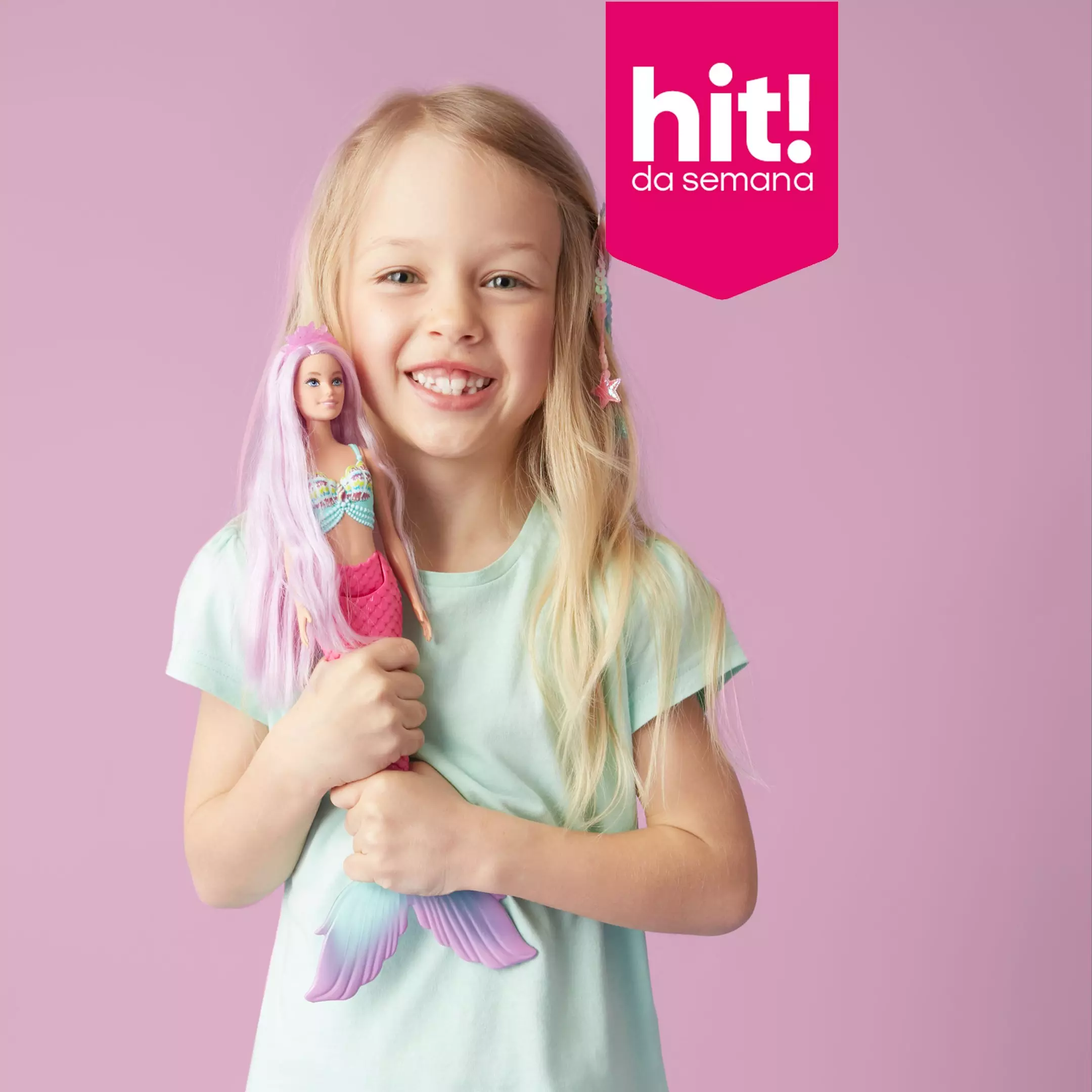 Menina sorridente a segurar uma boneca sereia com cabelo rosa, promoção hit da semana Pepco.