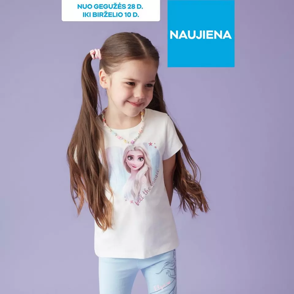 Mergaitė su ilgais plaukais šypsosi vilkėdama baltus Pepco marškinėlius su animacine princese ir karolių vėrinį.