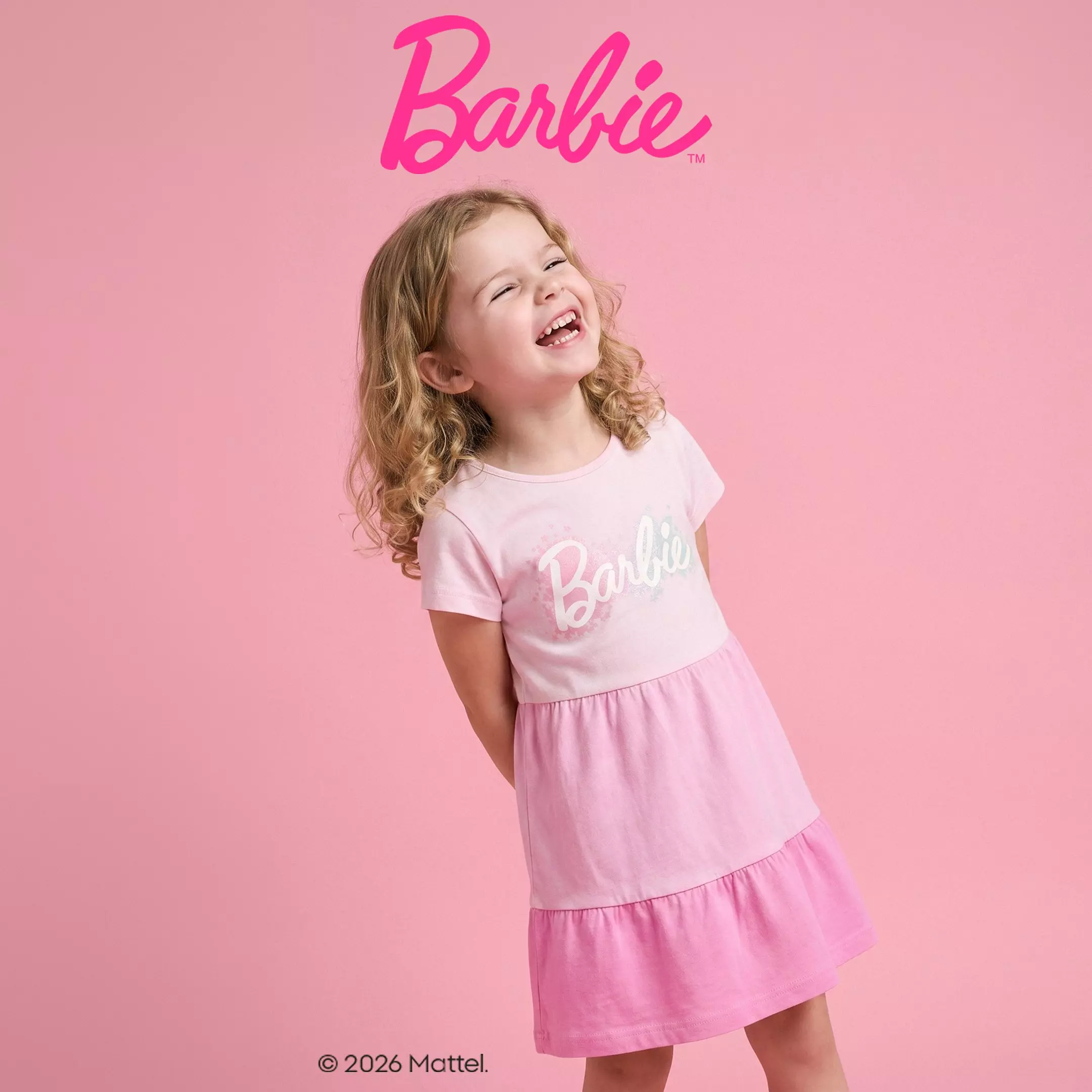 Niña sonriente con vestido rosa de Barbie de Pepco con volantes en tonos degradados.
